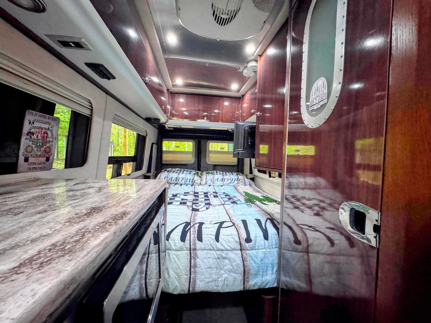 Explore in comfort! This RV rental features a cozy bed, kitchen counter, and scenic windows for your next camping trip.