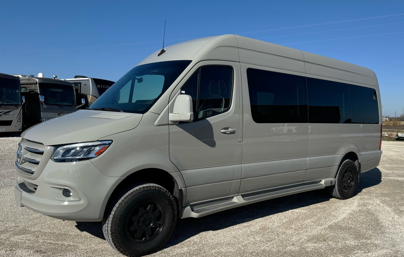 Light grey Mercedes Sprinter camper van, equipped for adventure, parked in an RV rental lot under blue skies.