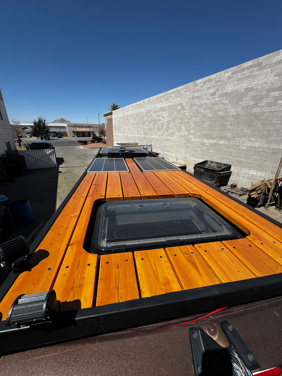 Top-down view of an RV rental roof featuring a wooden deck, skylight, and solar panels for off-grid adventures.