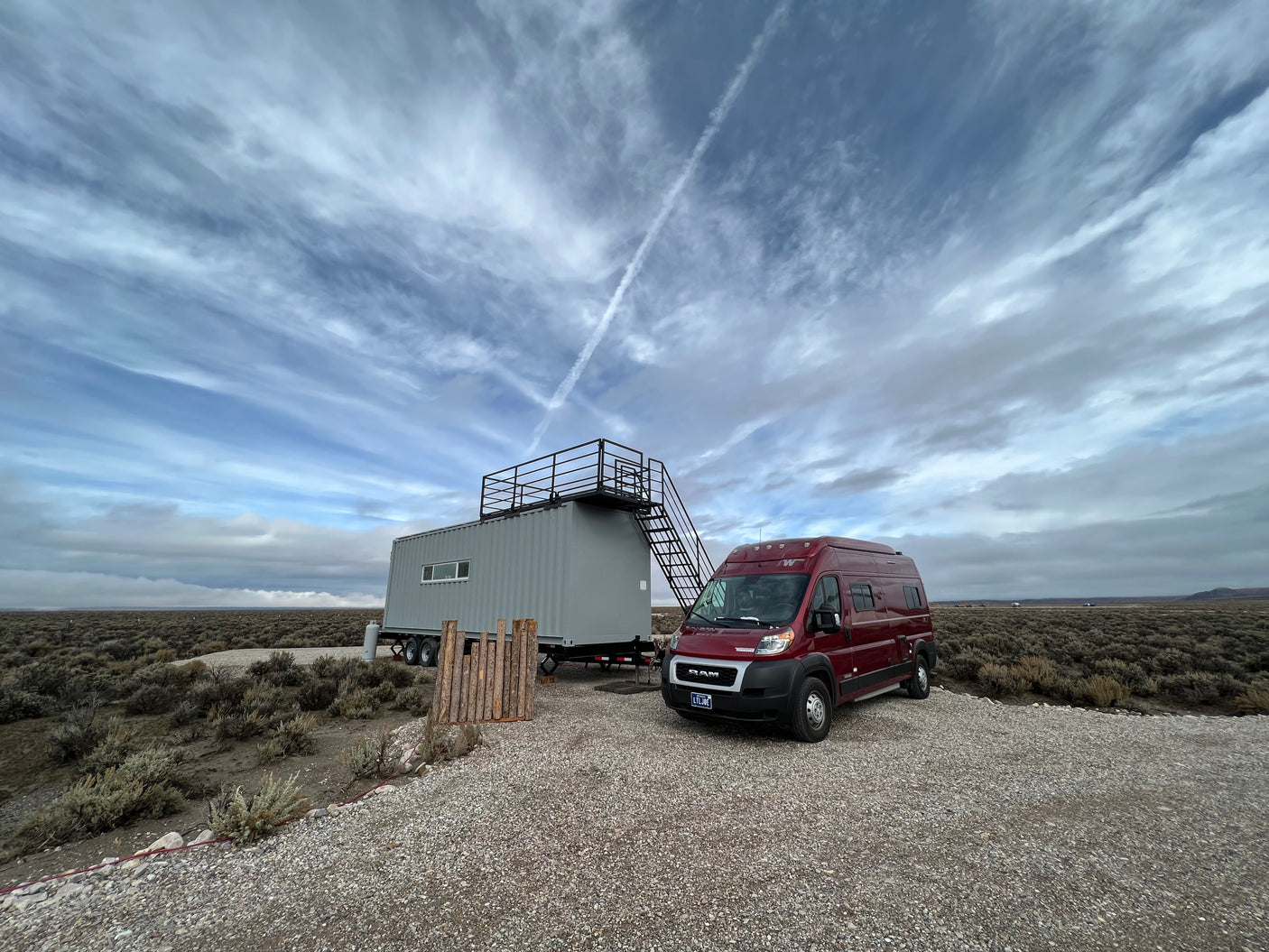 Explore the open landscape! An RV rental is parked next to a unique container home with a rooftop deck under a striking sky.