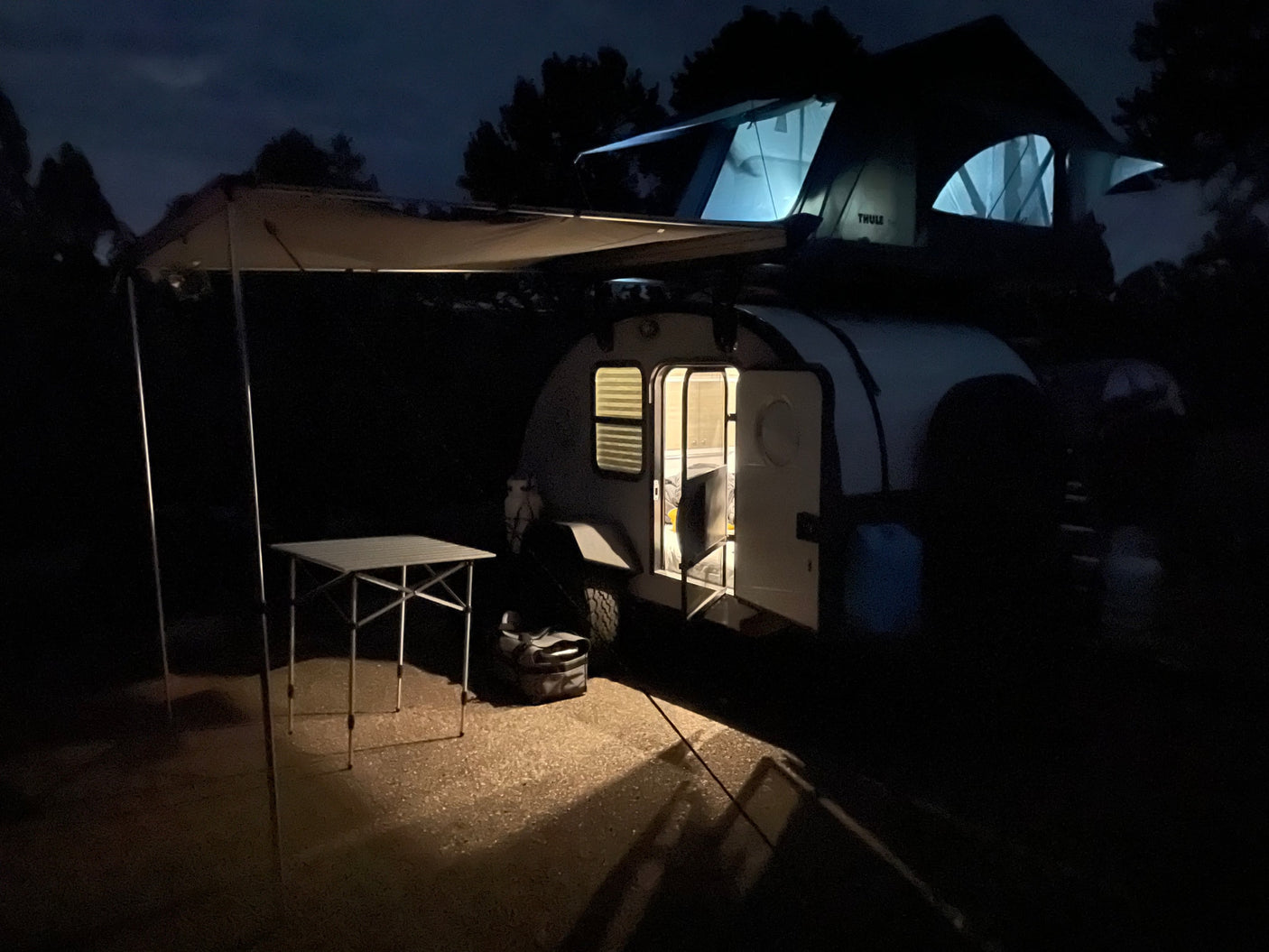 ideal for camping.|Sleek grey 'bean' teardrop camper with open door & Thule rooftop tent. Perfect RV rental for adventure.|RV rental interior: A cozy bedroom with a bed