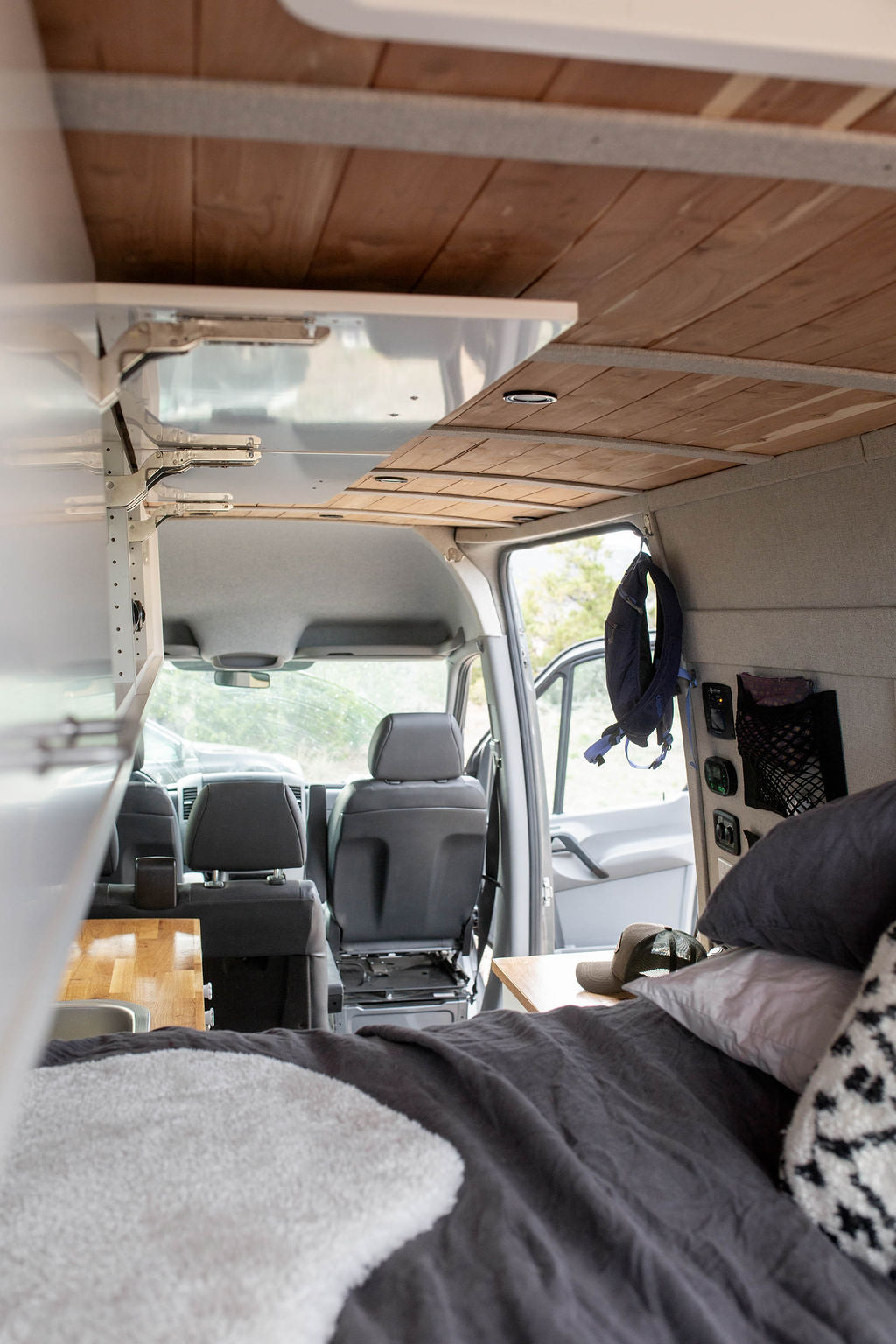 Cozy RV rental interior with a comfy bed, modern wood ceiling, and organized living space, ideal for van life adventures.