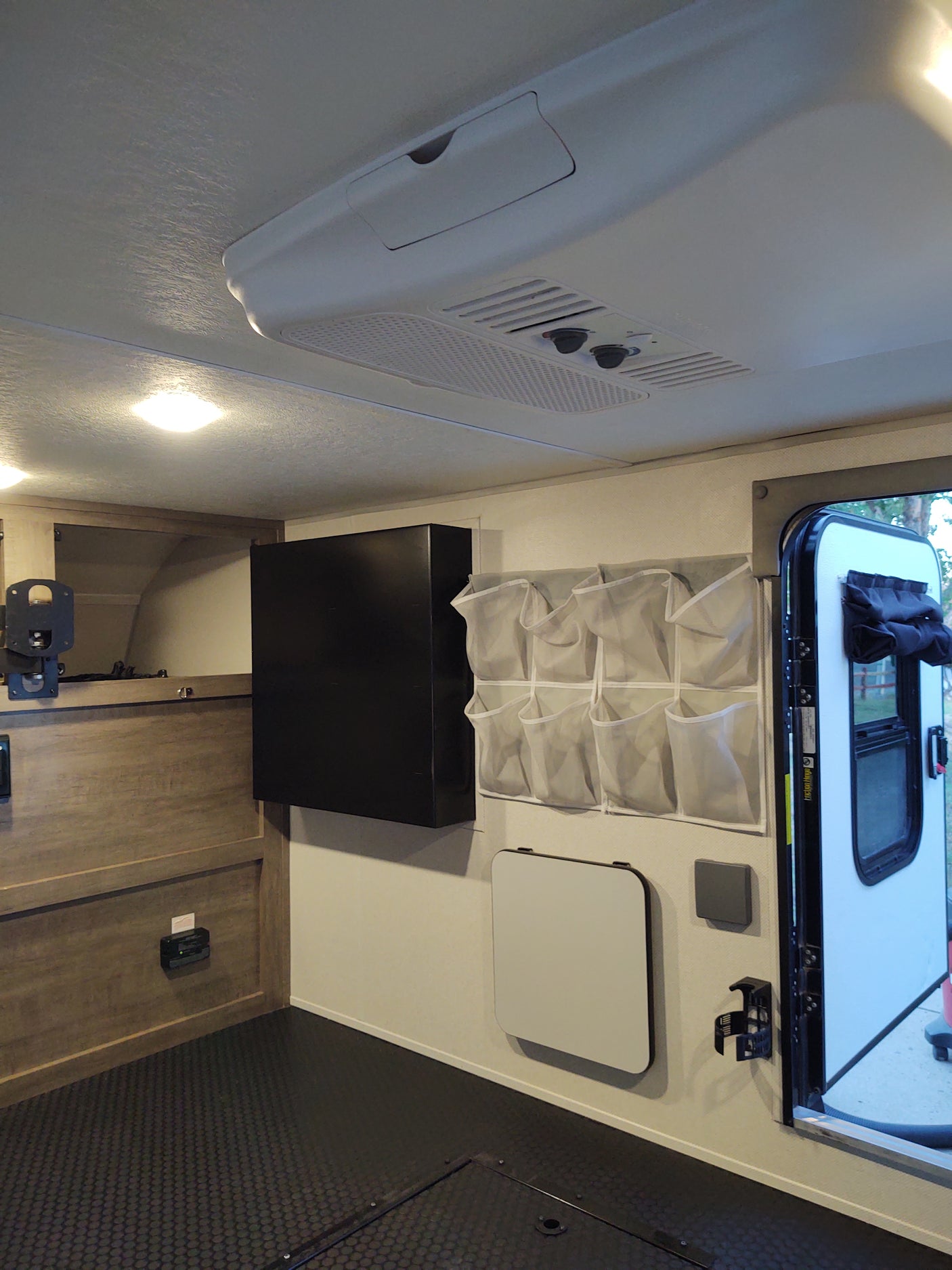 Interior of an RV rental, showing a window, overhead AC, wall-mounted storage, and a fold-down table for compact living.