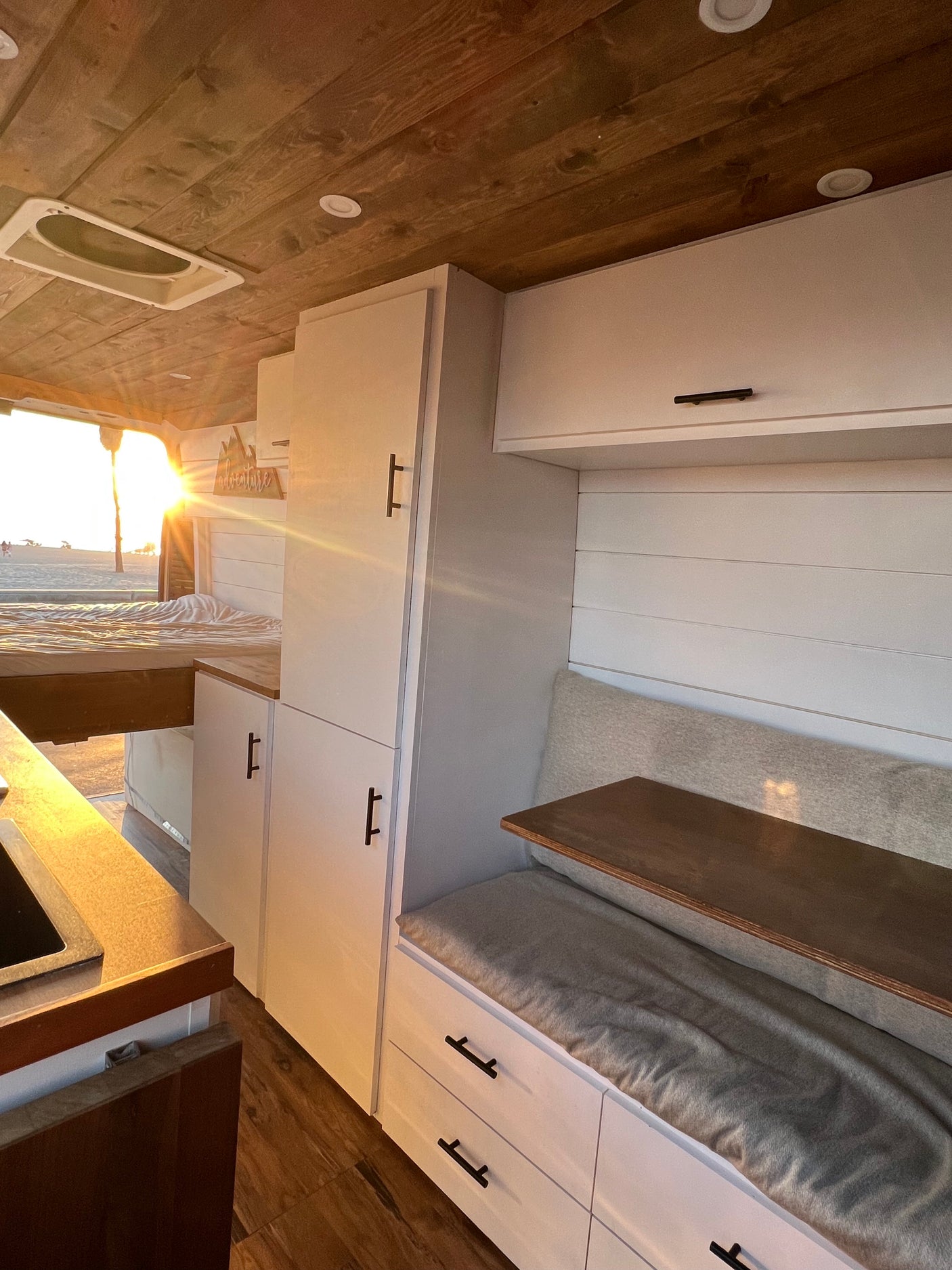 Step inside this custom RV rental: wood ceiling, white cabinets, and a stunning sunset over the beach from the back.