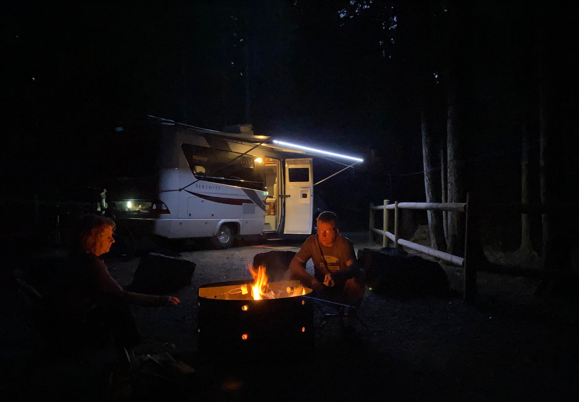 Nighttime camping by an RV rental. Two people relax by the fire pit's glow, ready for s'mores.