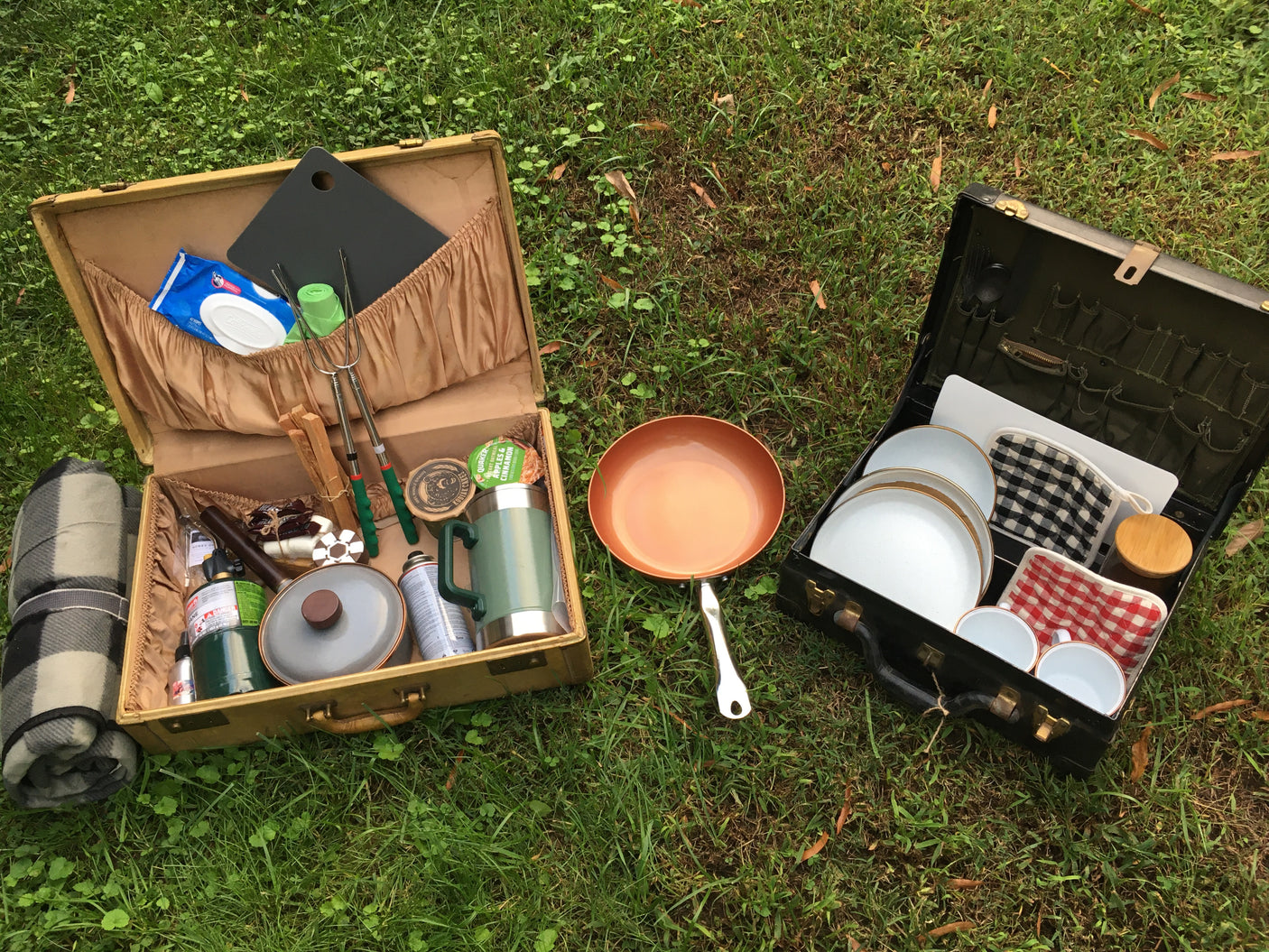 Organized RV rental picnic kit: Two open cases on grass reveal camping essentials, cooking ware, & dining sets for outdoor meals.