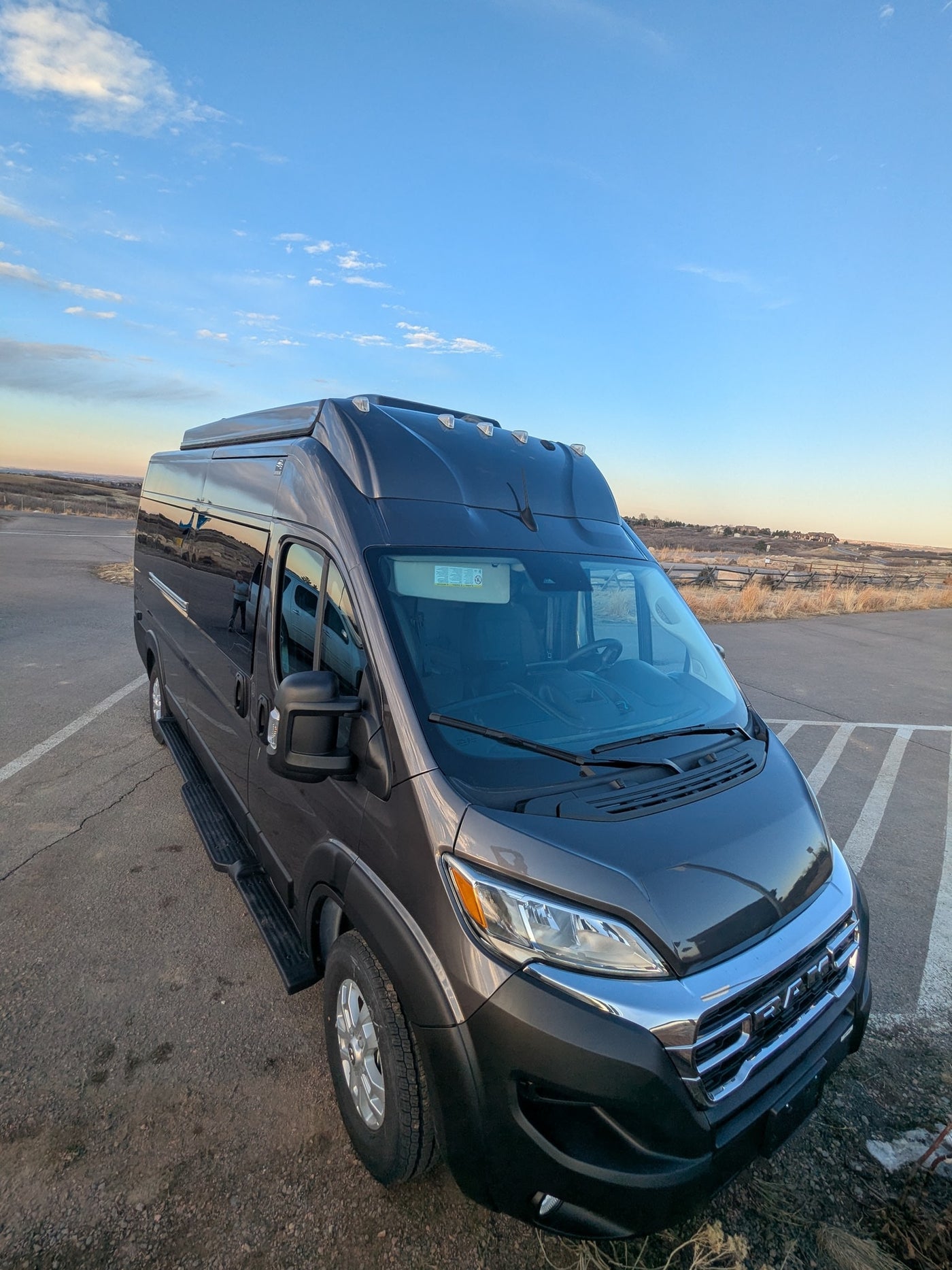Dark grey camper van with roof lights, perfect for an rv rental, parked in an outdoor lot under a clear blue sky. — photo 20