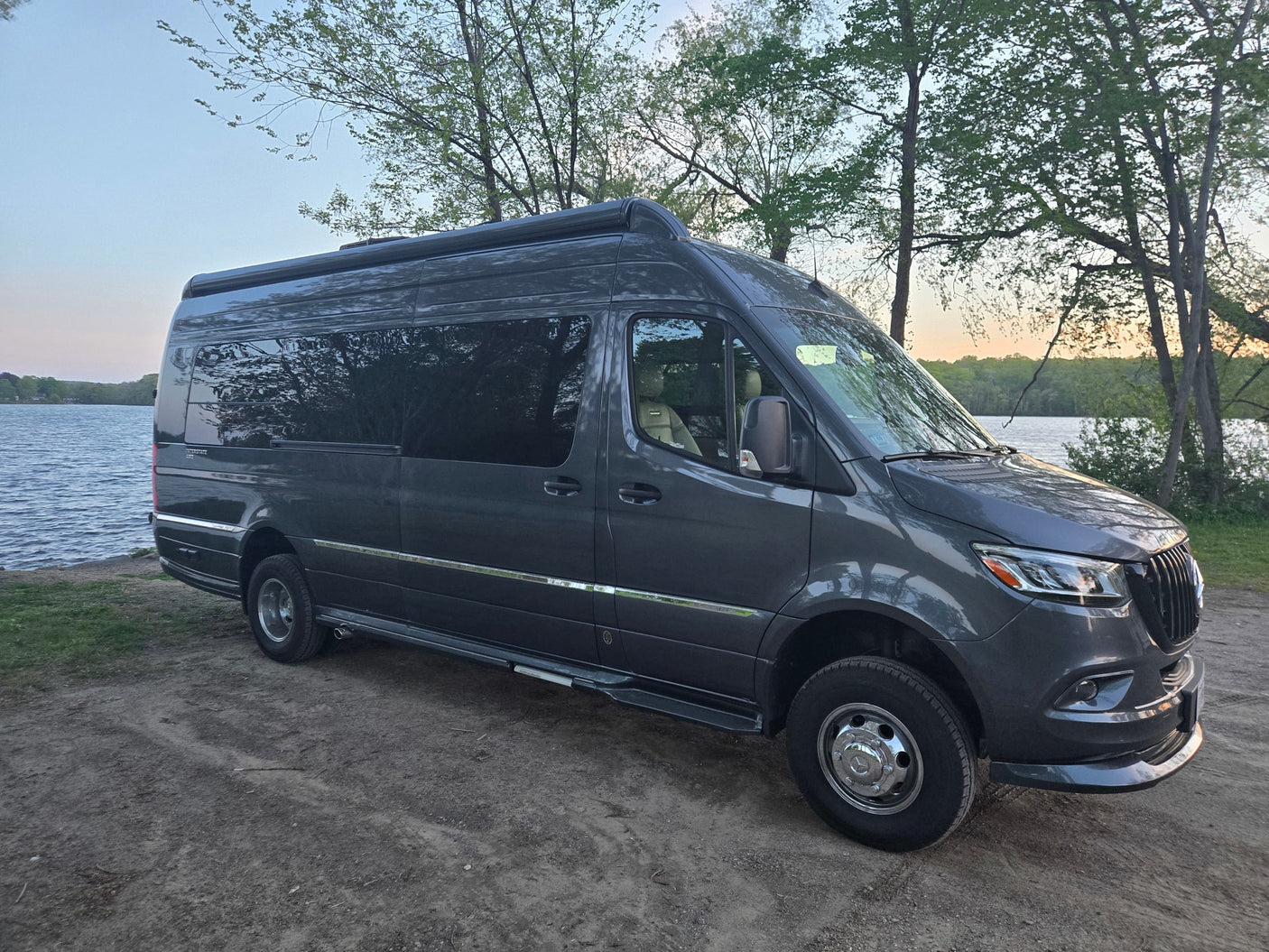 Dark grey Mercedes Sprinter camper van (RV rental) by a serene lake. Perfect for outdoor adventures and nature travel.