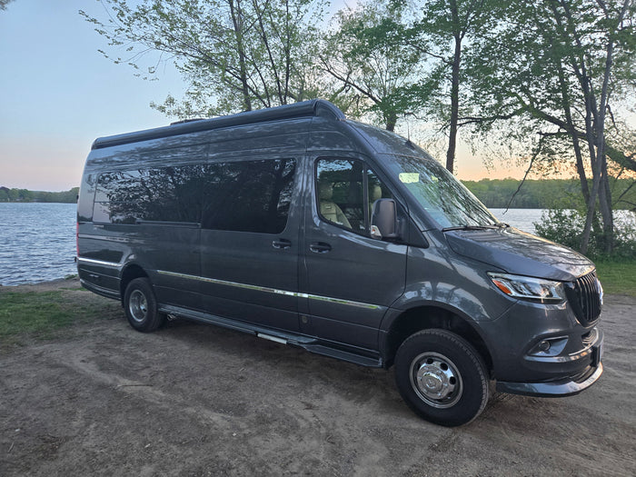 Dark grey Mercedes Sprinter camper van (RV rental) by a serene lake. Perfect for outdoor adventures and nature travel.