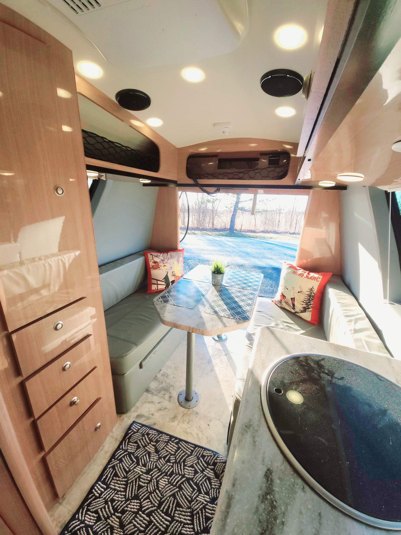Bright RV rental interior featuring a dinette, compact kitchen counter, and wooden storage for travelers.