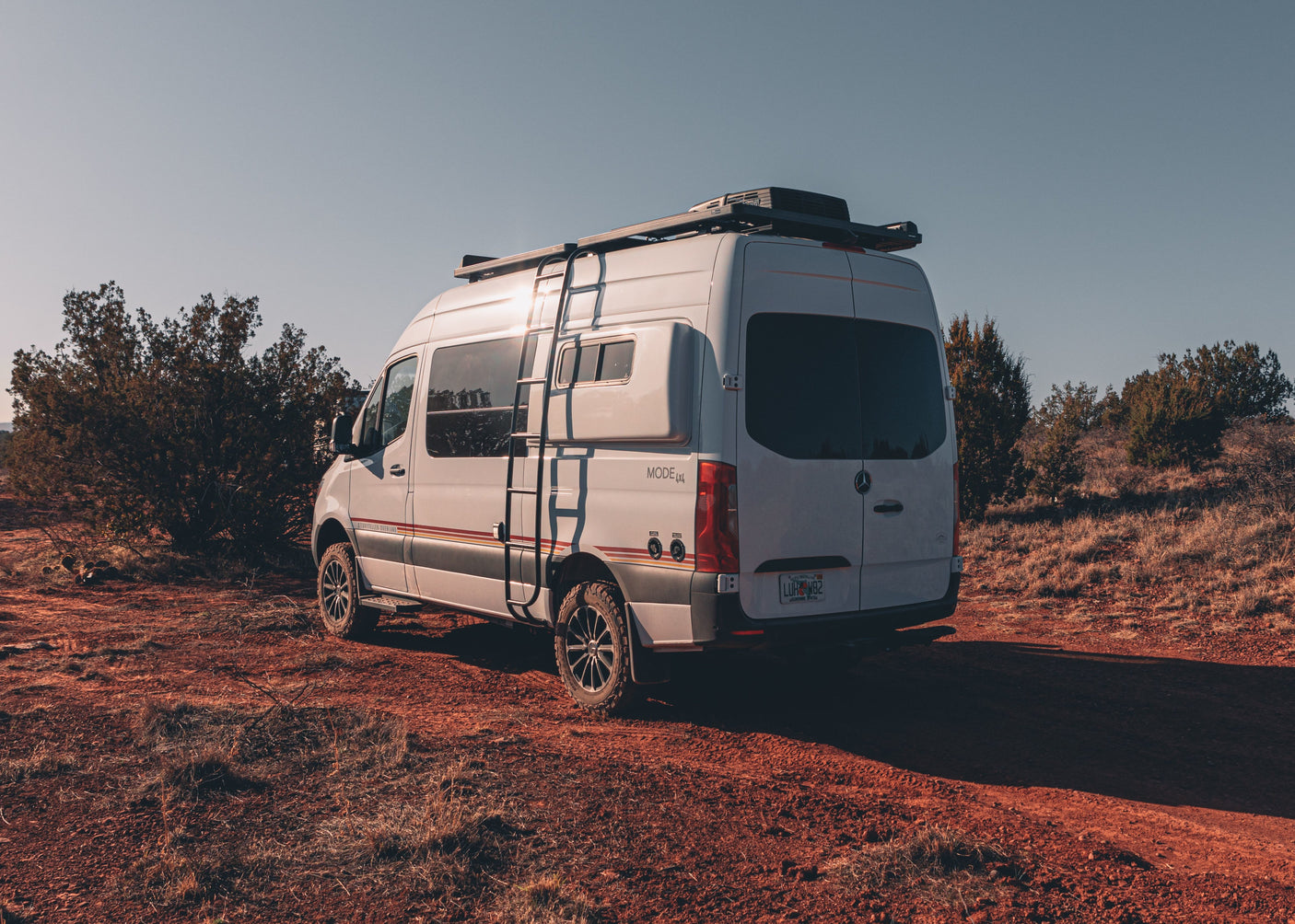 A white Storyteller Overland 4x4 RV rental van, a Mercedes Sprinter, parked on a red dirt trail.