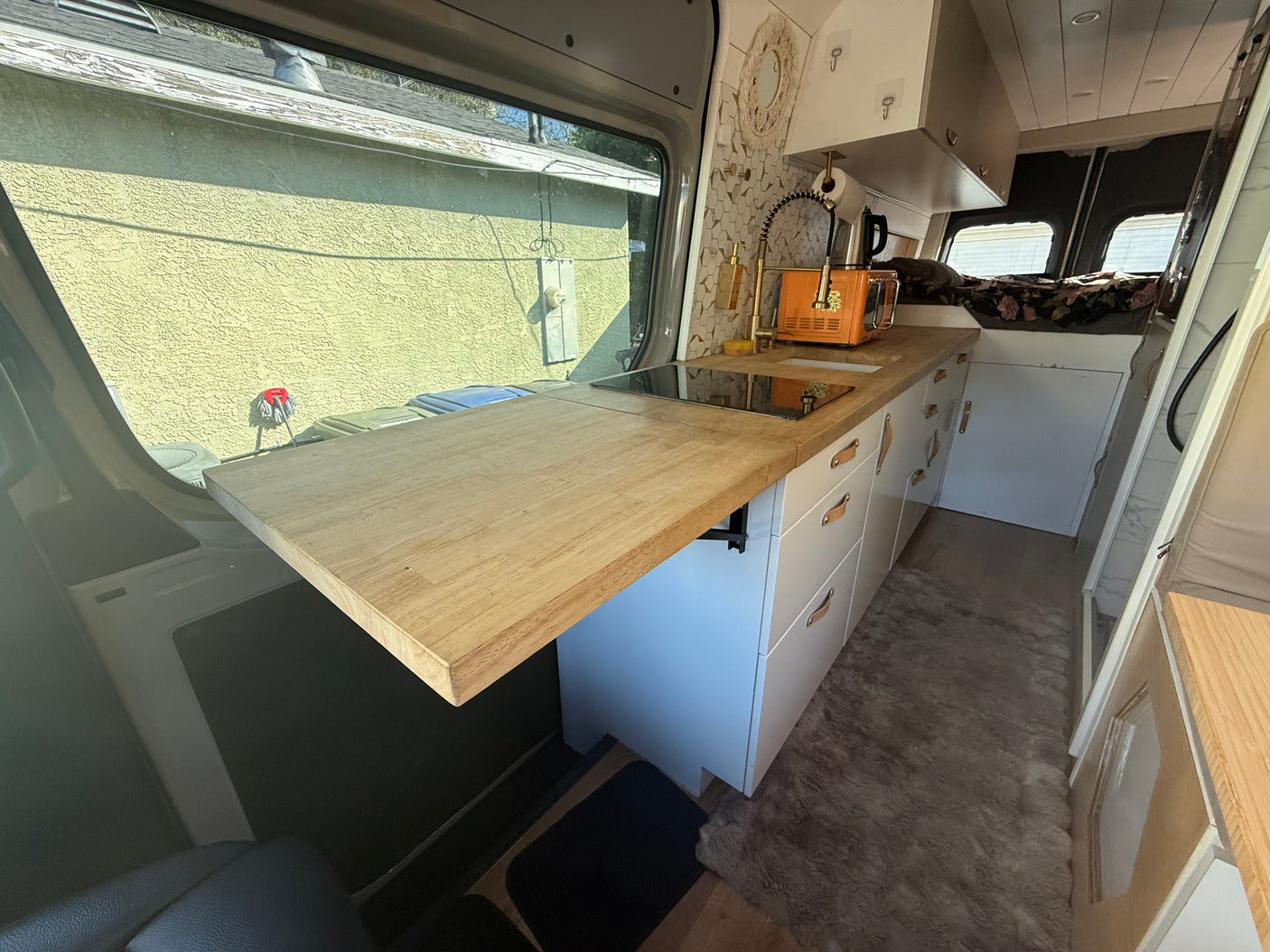RV rental: Stylish camper van interior with a modern kitchenette, wood counter, induction cooktop, and bed area.