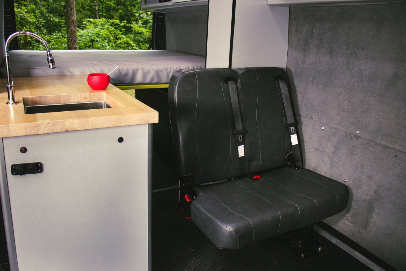 RV rental camper van interior showing kitchen sink, bed, & passenger seating. Perfect for travel!