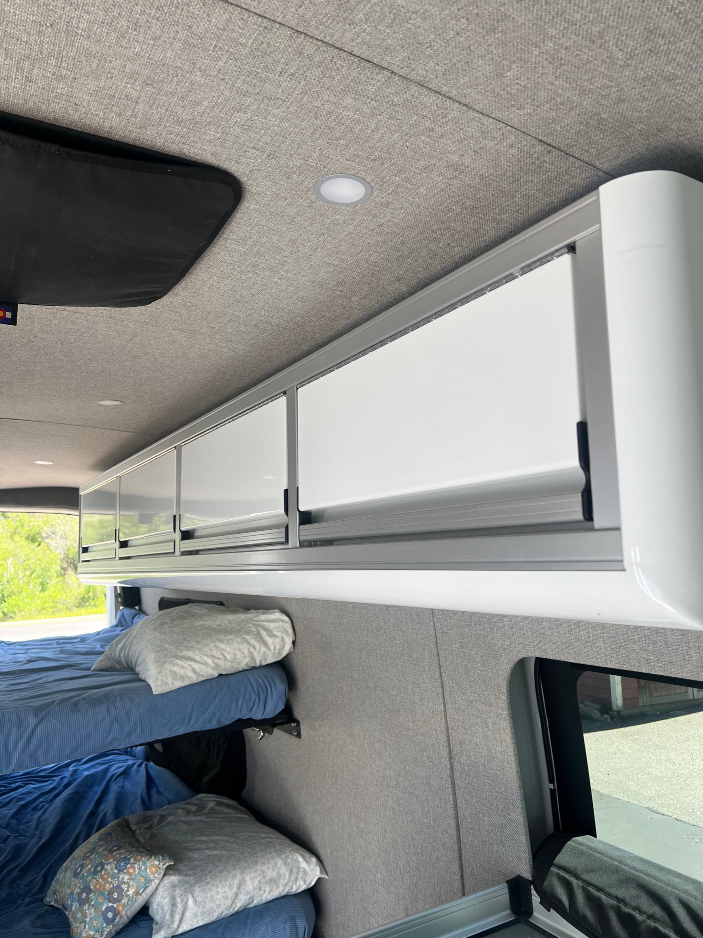 Inside a modern RV rental: bunk beds, bright overhead cabinets, and soft upholstered walls/ceiling.
