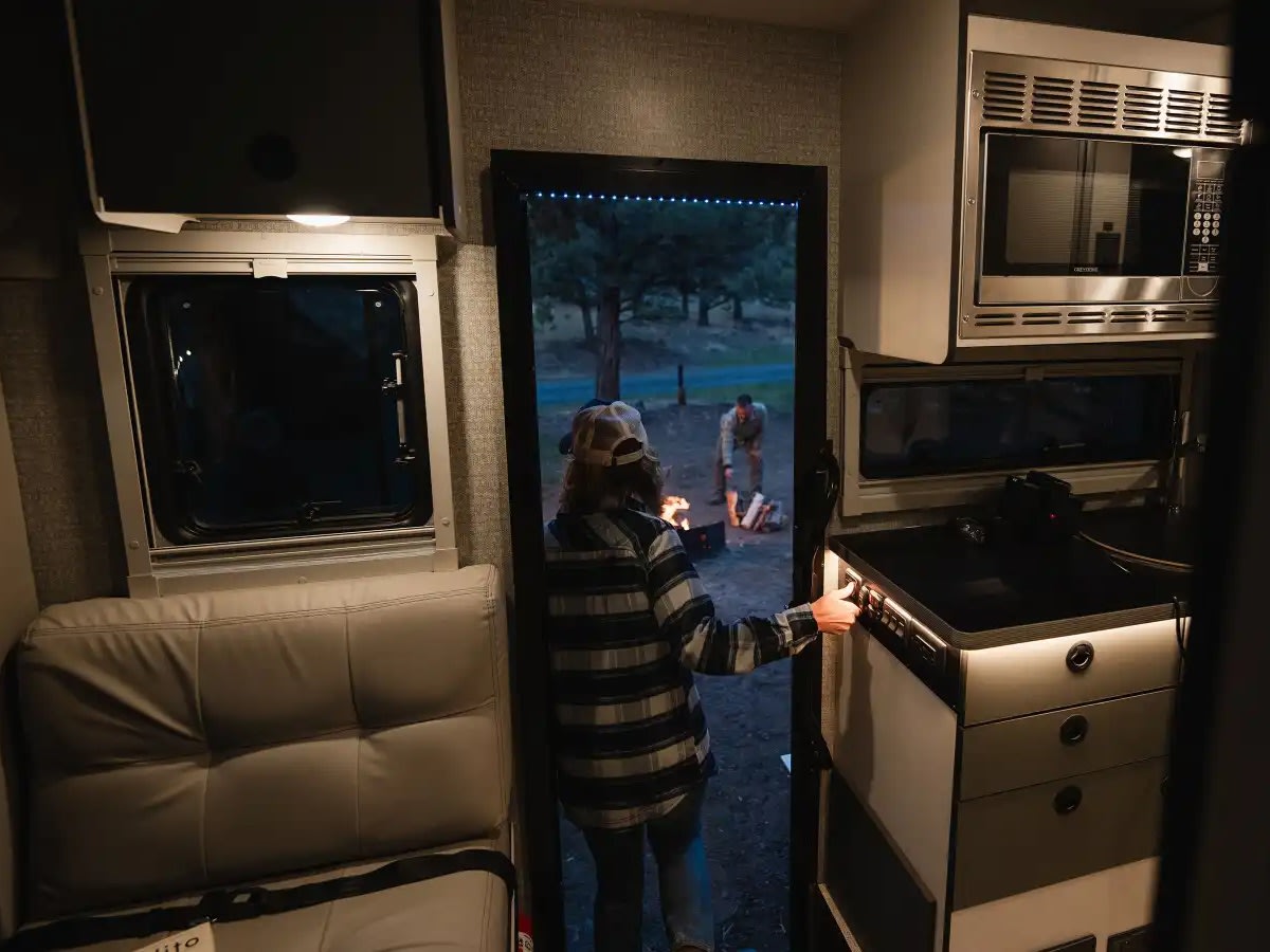 and forest views from large windows.|This modern RV rental's interior shows a bed lifted for under-bed storage — photo 15