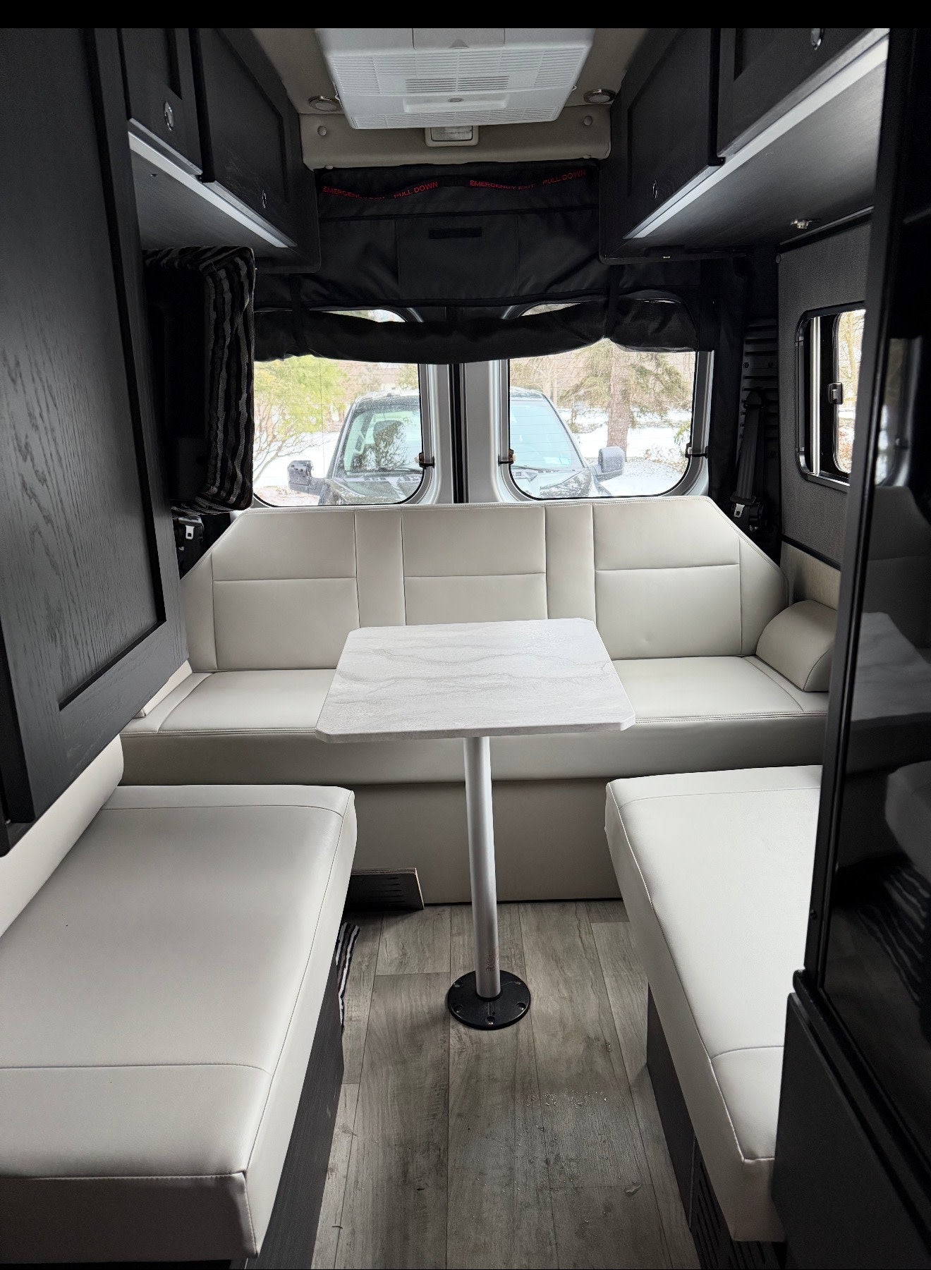 Modern rv rental interior: bright white dinette seating, central table, overhead storage, and rear windows. — photo 6
