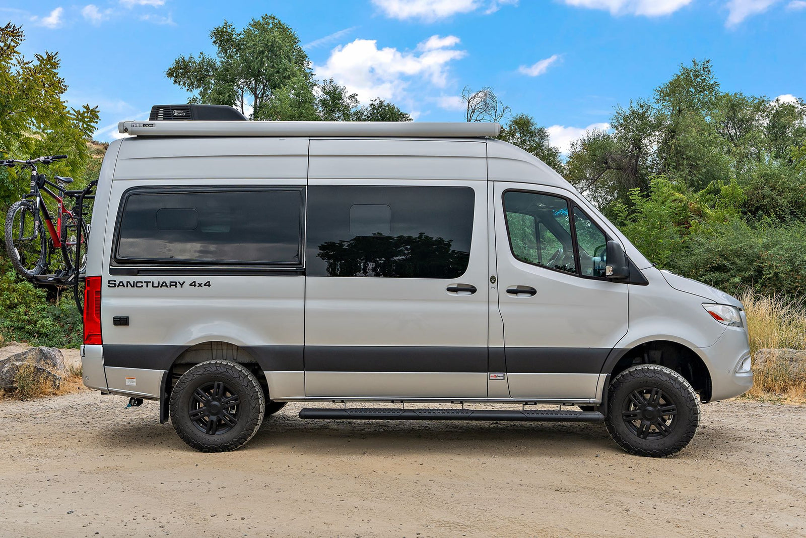 Silver Sanctuary 4x4 Sprinter camper van with bikes, parked on dirt road. Perfect RV rental for adventures.