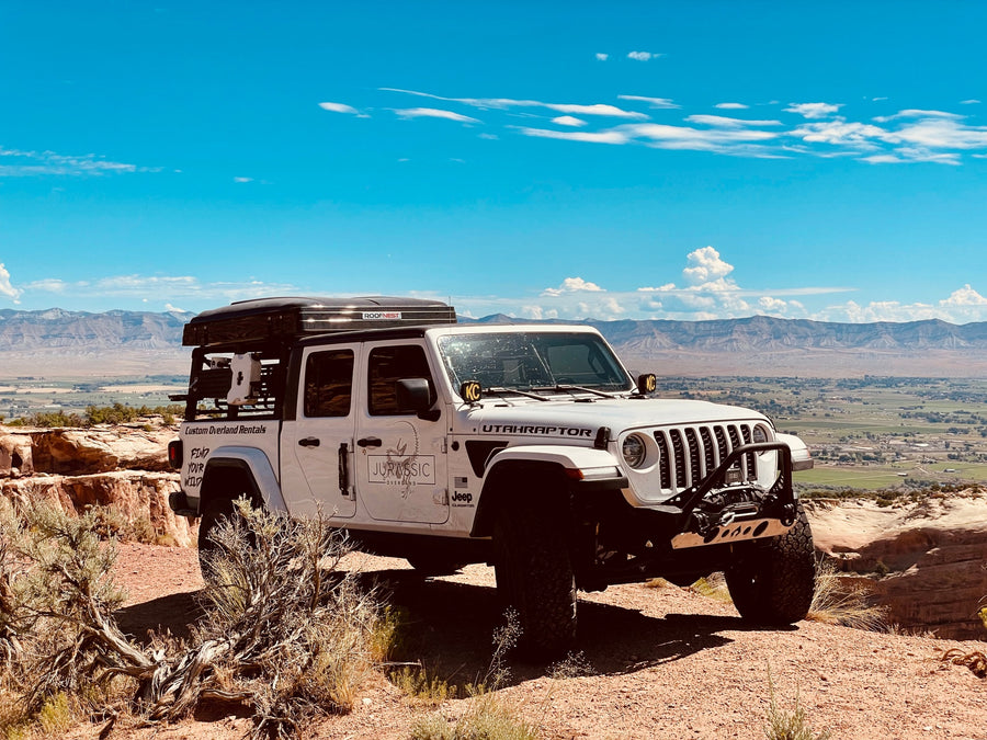 and table set up on a dirt site.|Custom RV rental Jeep Gladiator with rooftop tent ready for overlanding