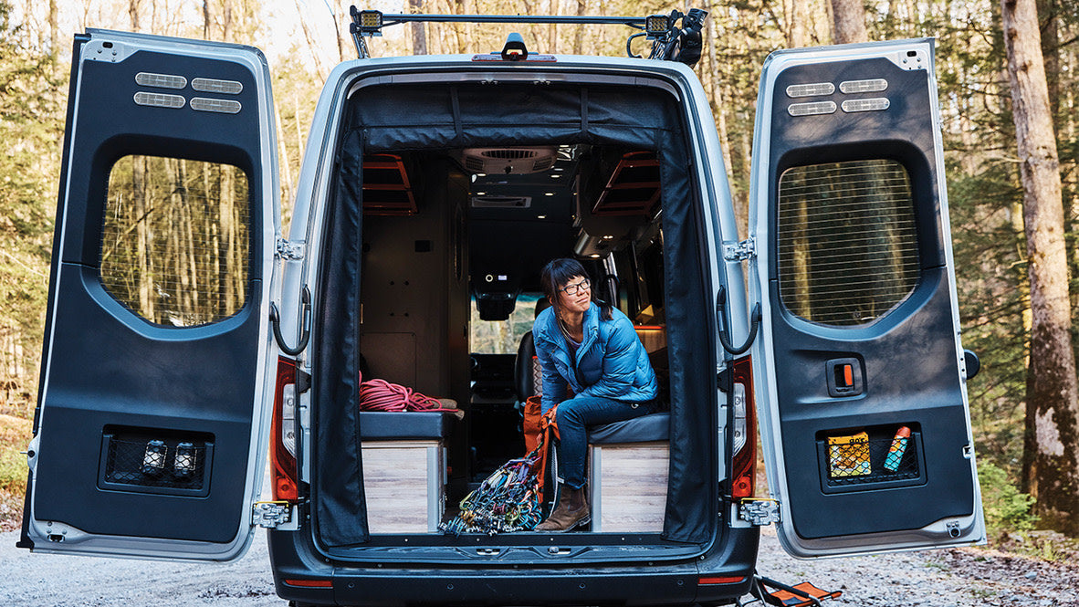 Experience van life with rv rental. Woman relaxing inside a converted camper van, surrounded by nature and climbing gear.