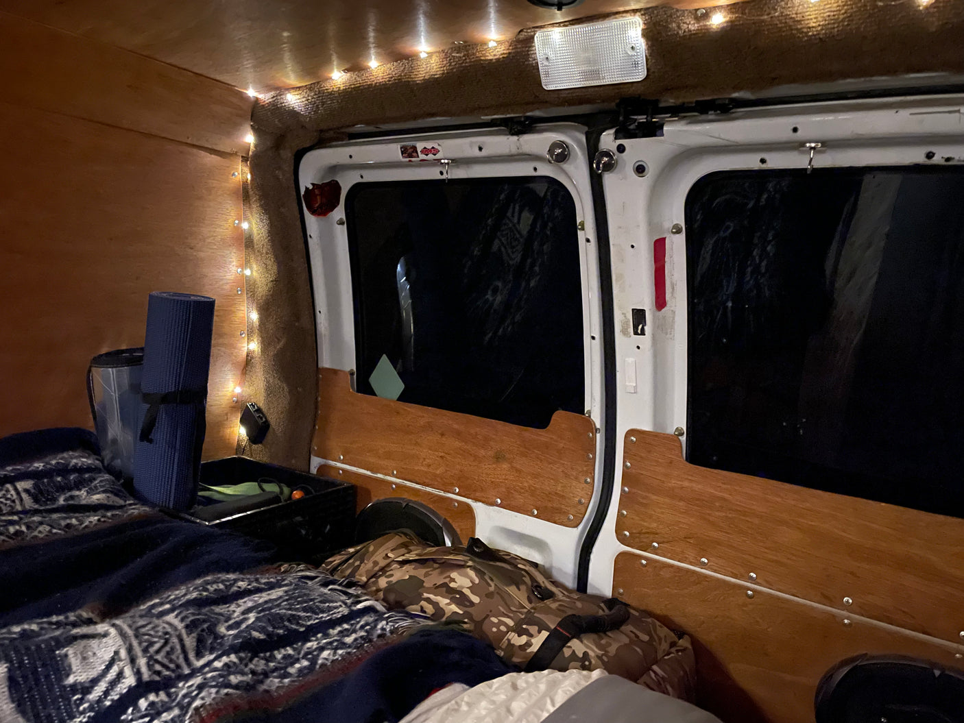 Inside a cozy RV rental: a comfortable sleeping setup with string lights, wooden walls, and a bed.