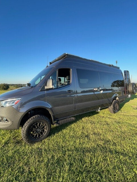 perfect for rv rental adventures on grass under a blue sky.|A dark grey Mercedes Sprinter camper van