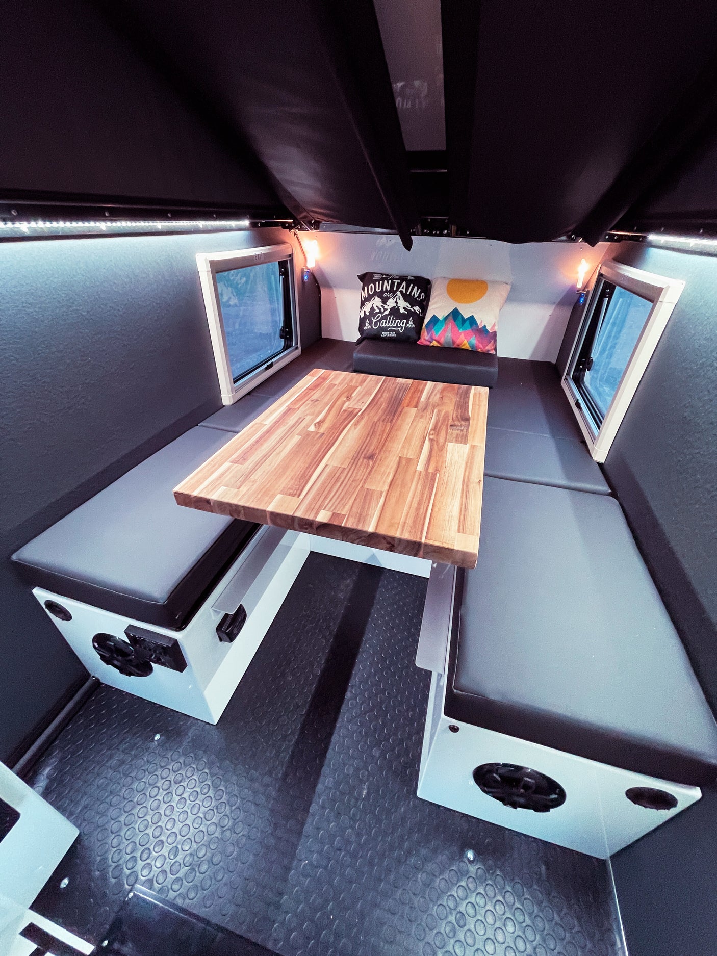 Compact RV rental interior featuring a wood dinette, bench seating, and LED lighting for cozy adventures.