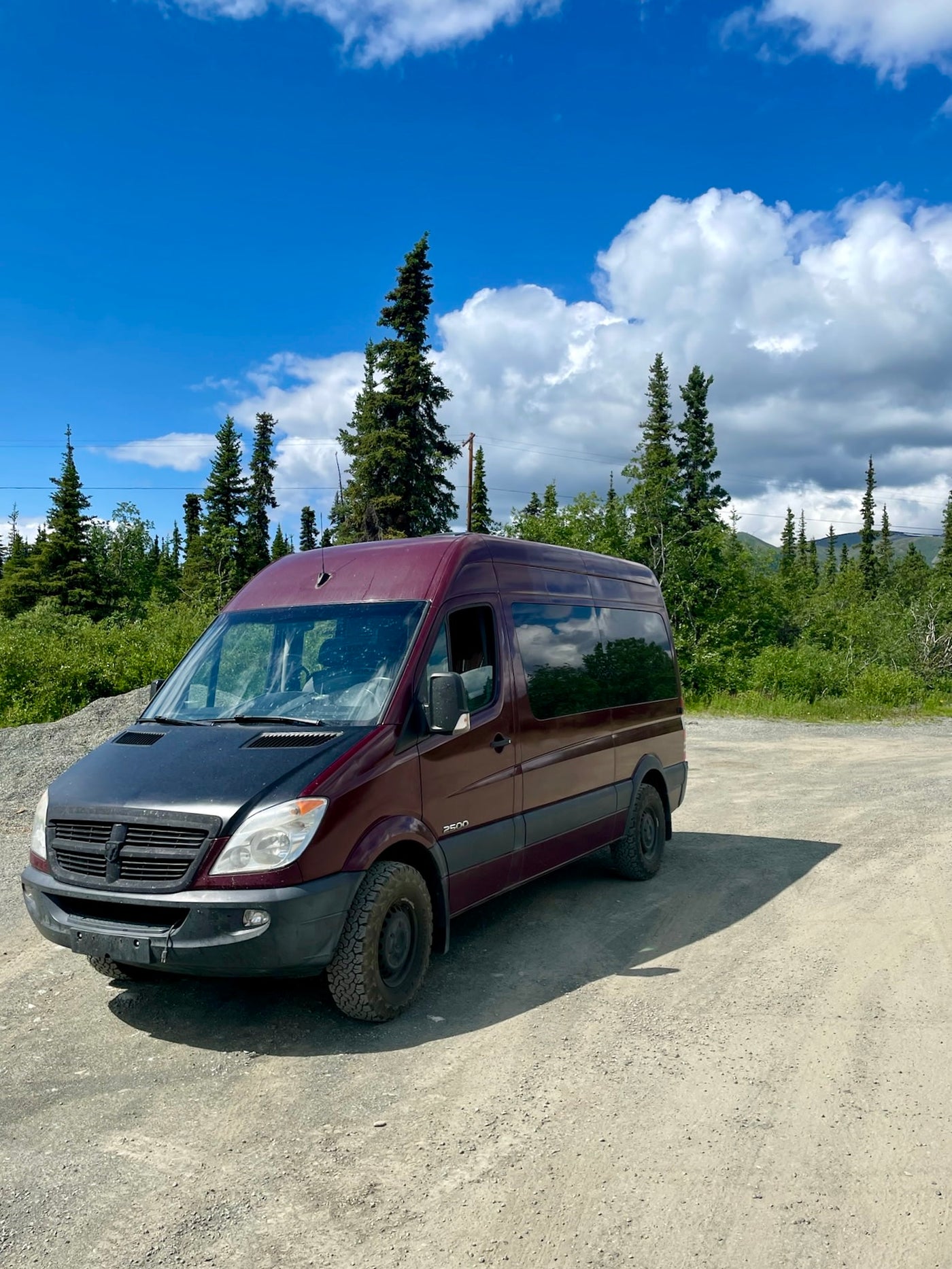 Maroon Dodge Sprinter camper van with black hood on a gravel road — photo 1