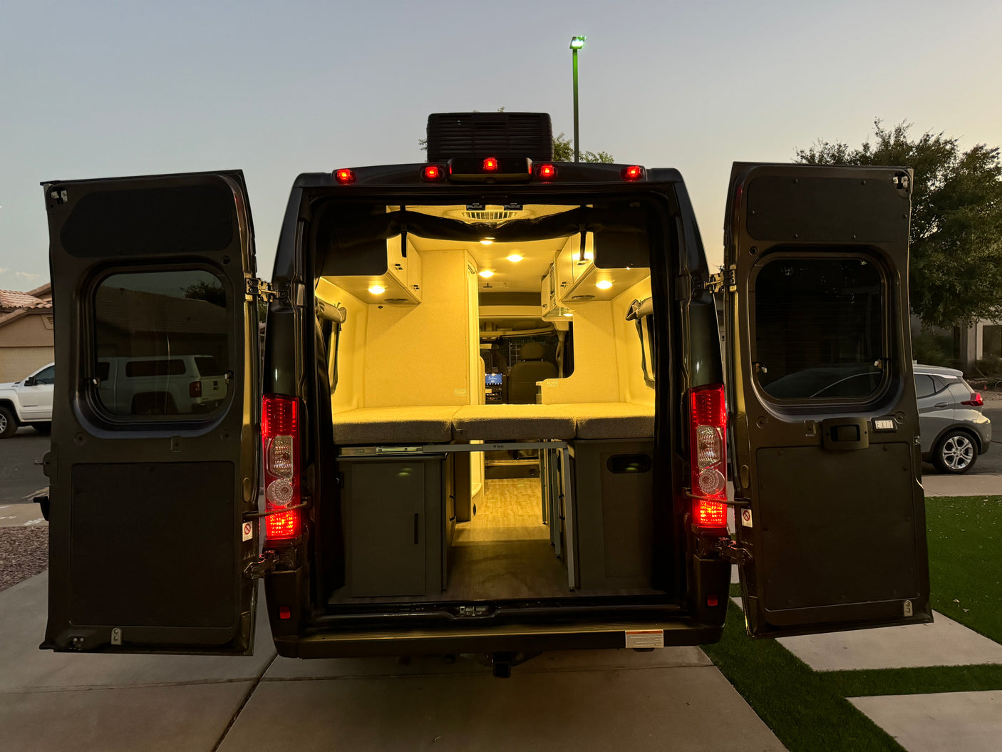 Explore a modern camper van RV rental interior at dusk: illuminated bed, cabinets, and amenities through open rear doors.