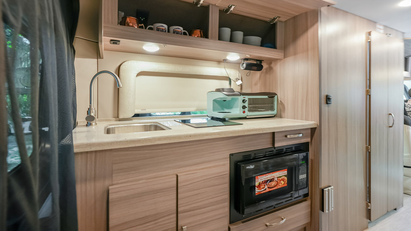 A bright, well-appointed RV rental kitchen features a sink, microwave, toaster oven, coffee maker, and ample storage.