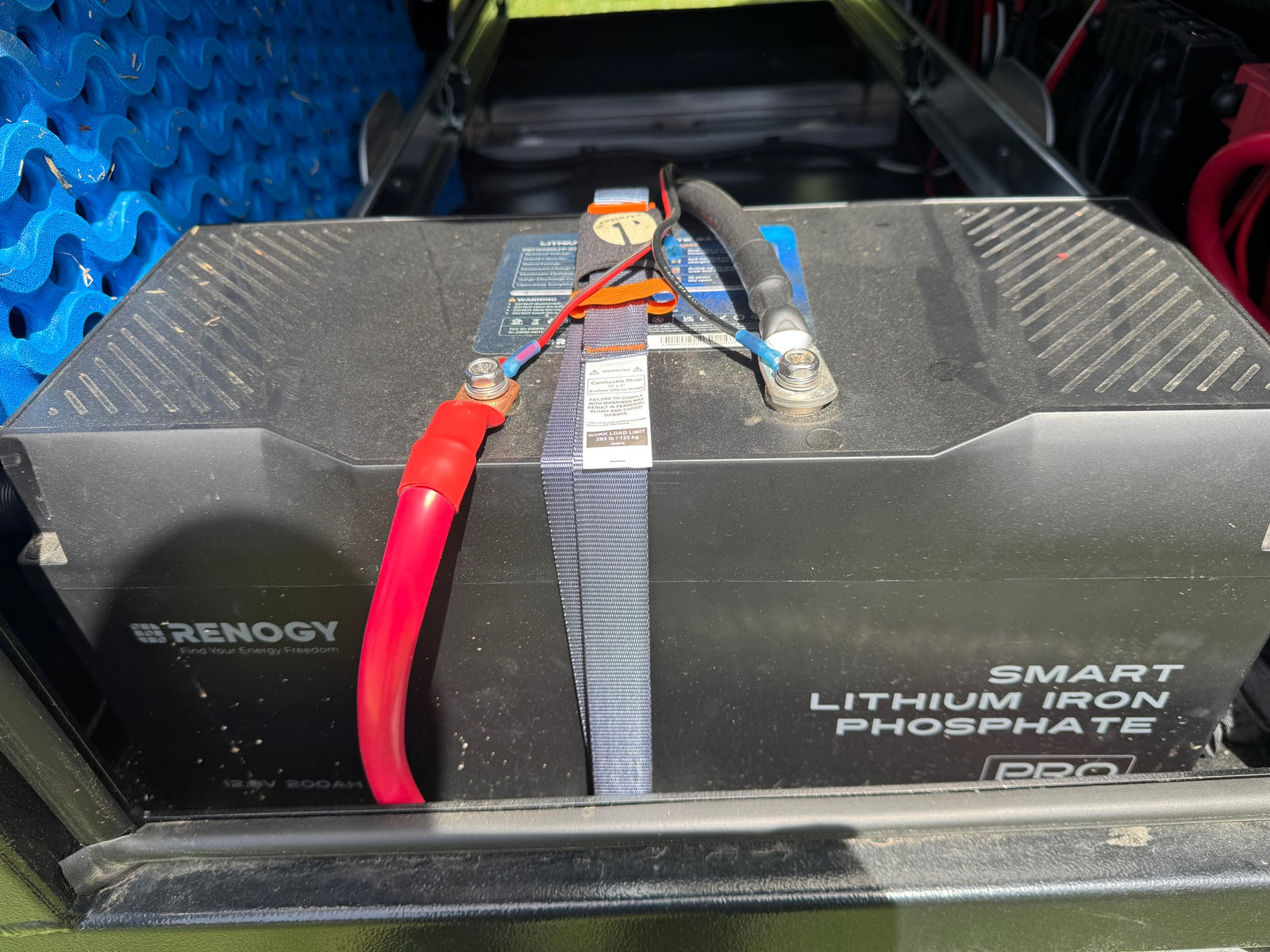 A Renogy 12.8V 200AH lithium battery secured for an RV rental, providing reliable off-grid power. Shows connections and strap.
