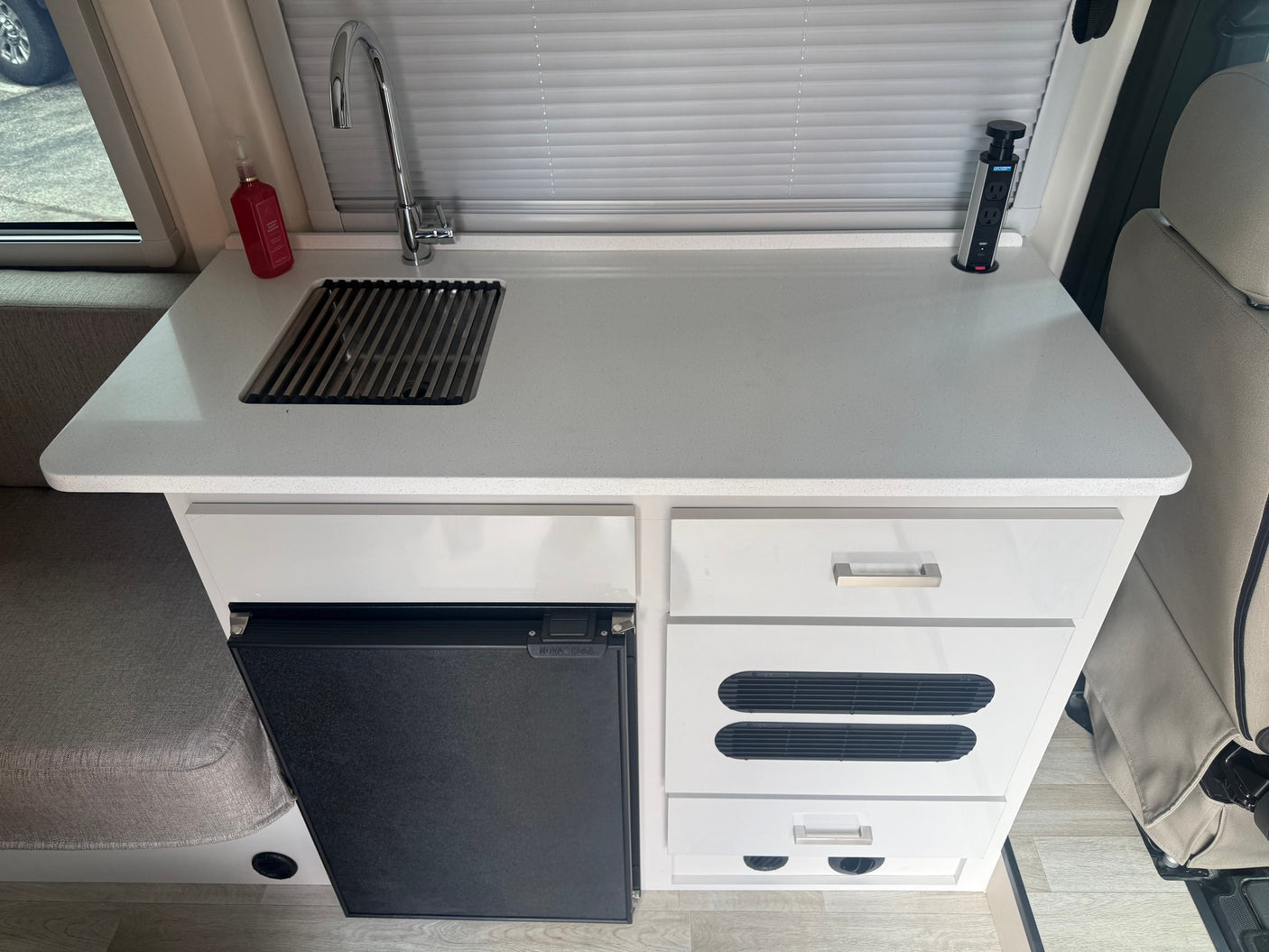Efficient RV rental kitchen featuring a white countertop, sink, NOVAKOOL fridge, and a pop-up power station for your journey.