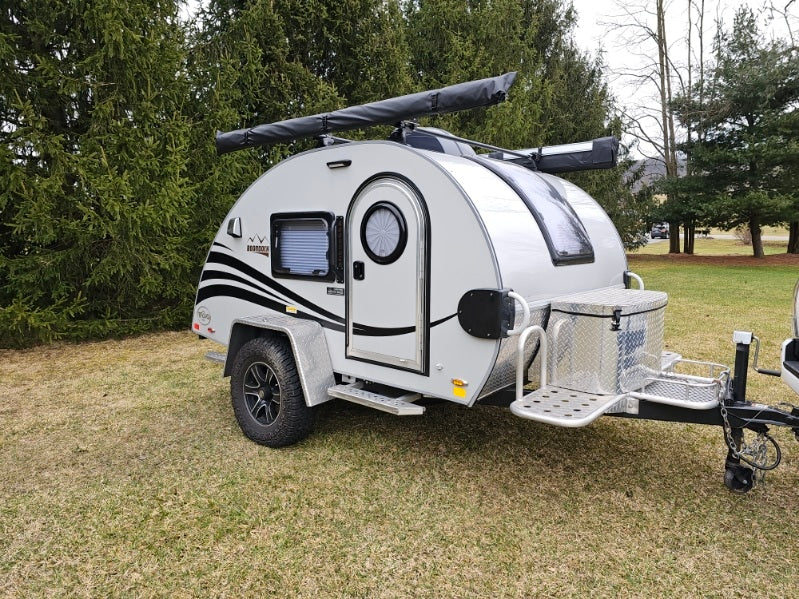 This compact teardrop travel trailer, ideal for rv rental, features a unique round door, roof awning, and front storage box.
