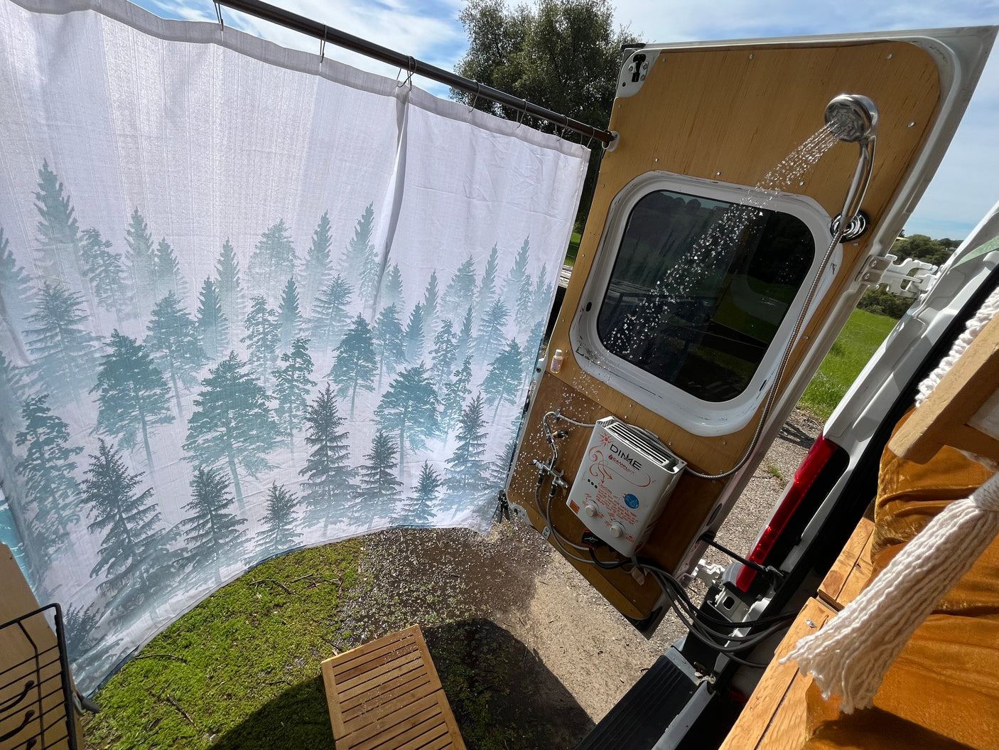 Experience an outdoor RV rental shower! This setup features a forest curtain, hot water heater, & spray from the van's rear.
