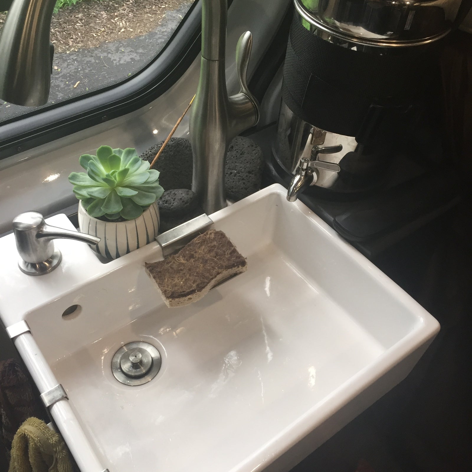 Bright sink with soap, sponge, and plant in an RV rental. Modern faucet and compact design for on-the-go living.
