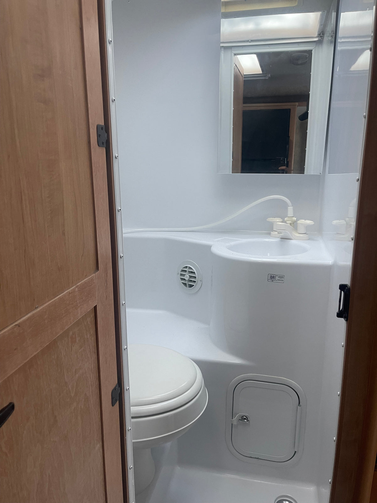 Compact RV rental wet bath, featuring an integrated sink with shower faucet, toilet, and storage hatch. — photo 8