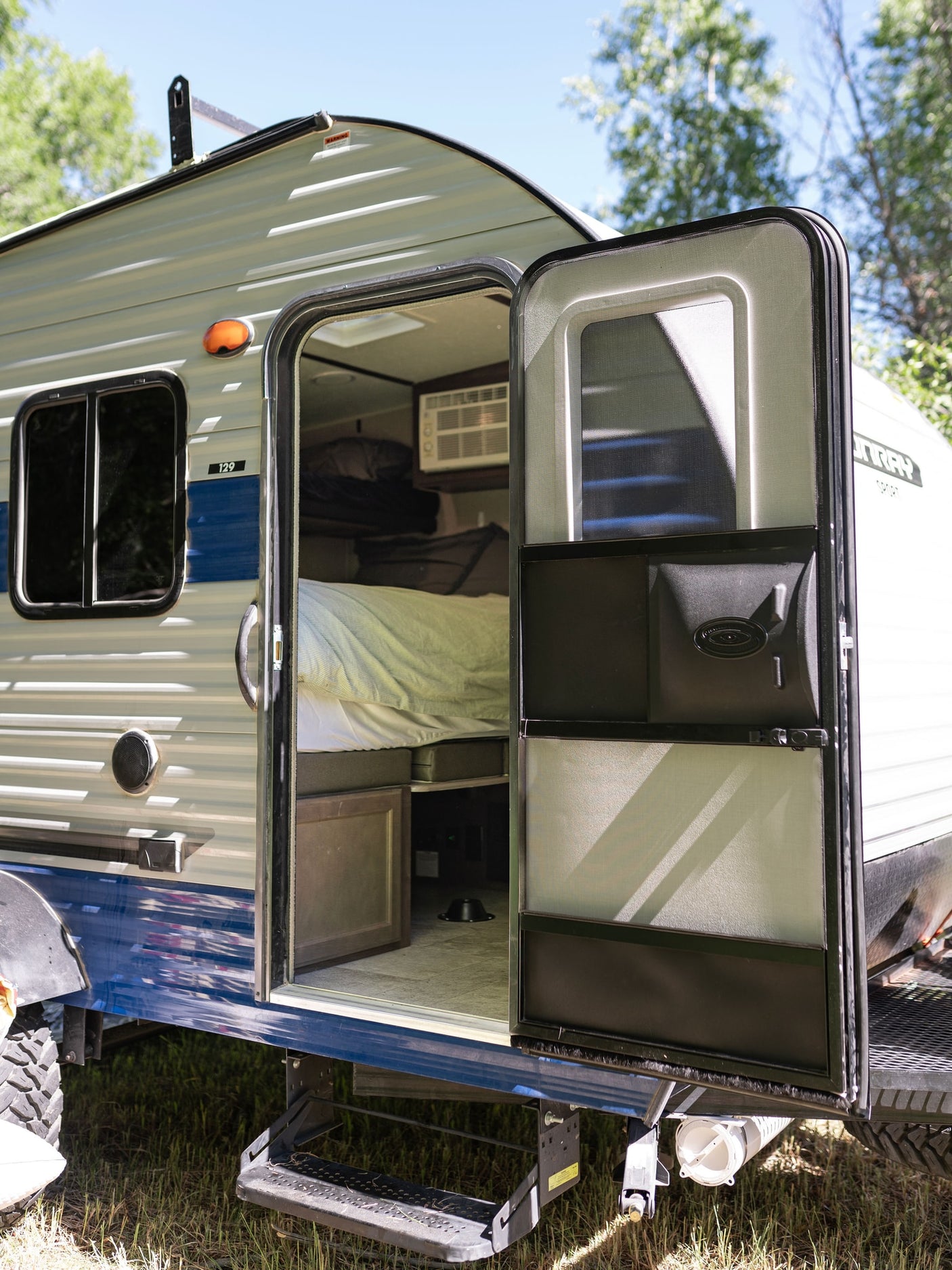 Open door of a compact rv rental camper with an interior bed and A/C unit, ready for your camping adventure.