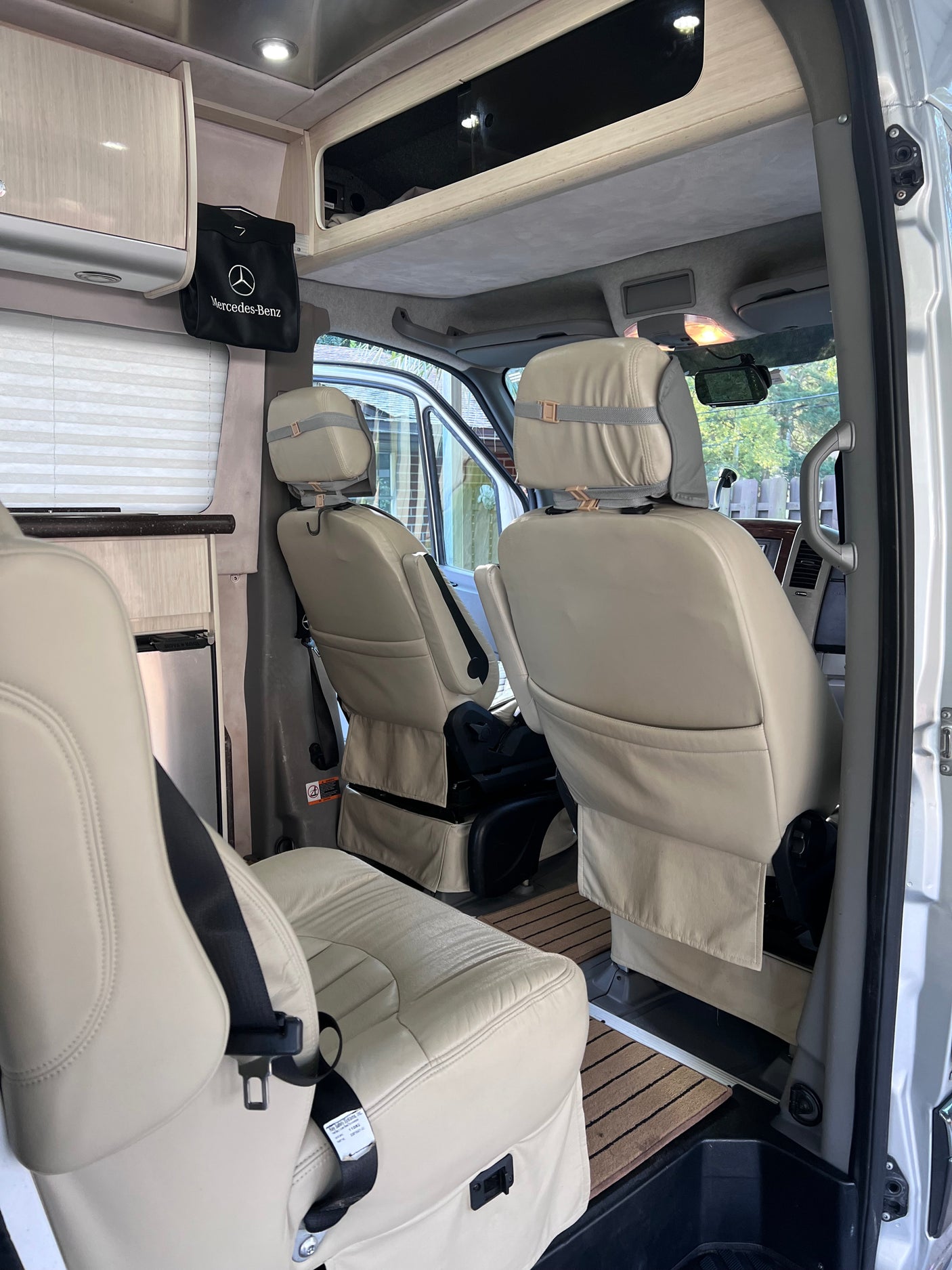 View inside an RV rental showing cream leather seats, overhead storage, and a small fridge. This comfortable cabin is ready for travel.