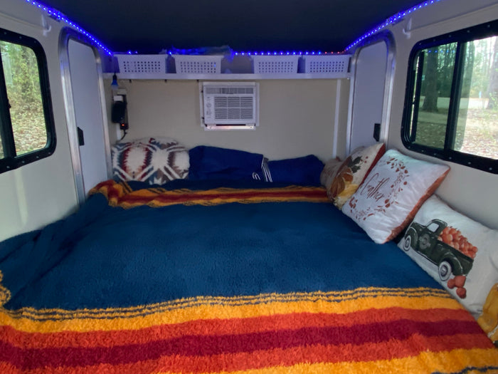 and a fire pit.|Experience nature with this rv rental! A cozy teardrop camper with its door open reveals a bed
