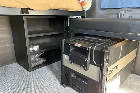 RV rental interior: under-bed storage shelves & an ARB ZERO portable fridge on carpeted floor.