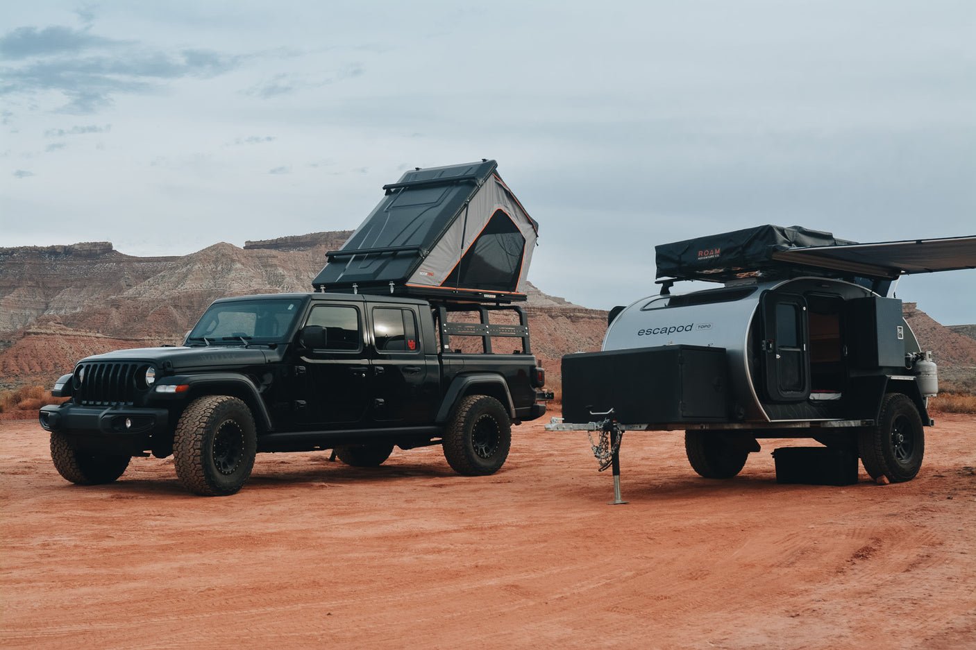 Off-road RV rental adventure: Jeep Gladiator with open rooftop tent & teardrop trailer with awning, in a desert.