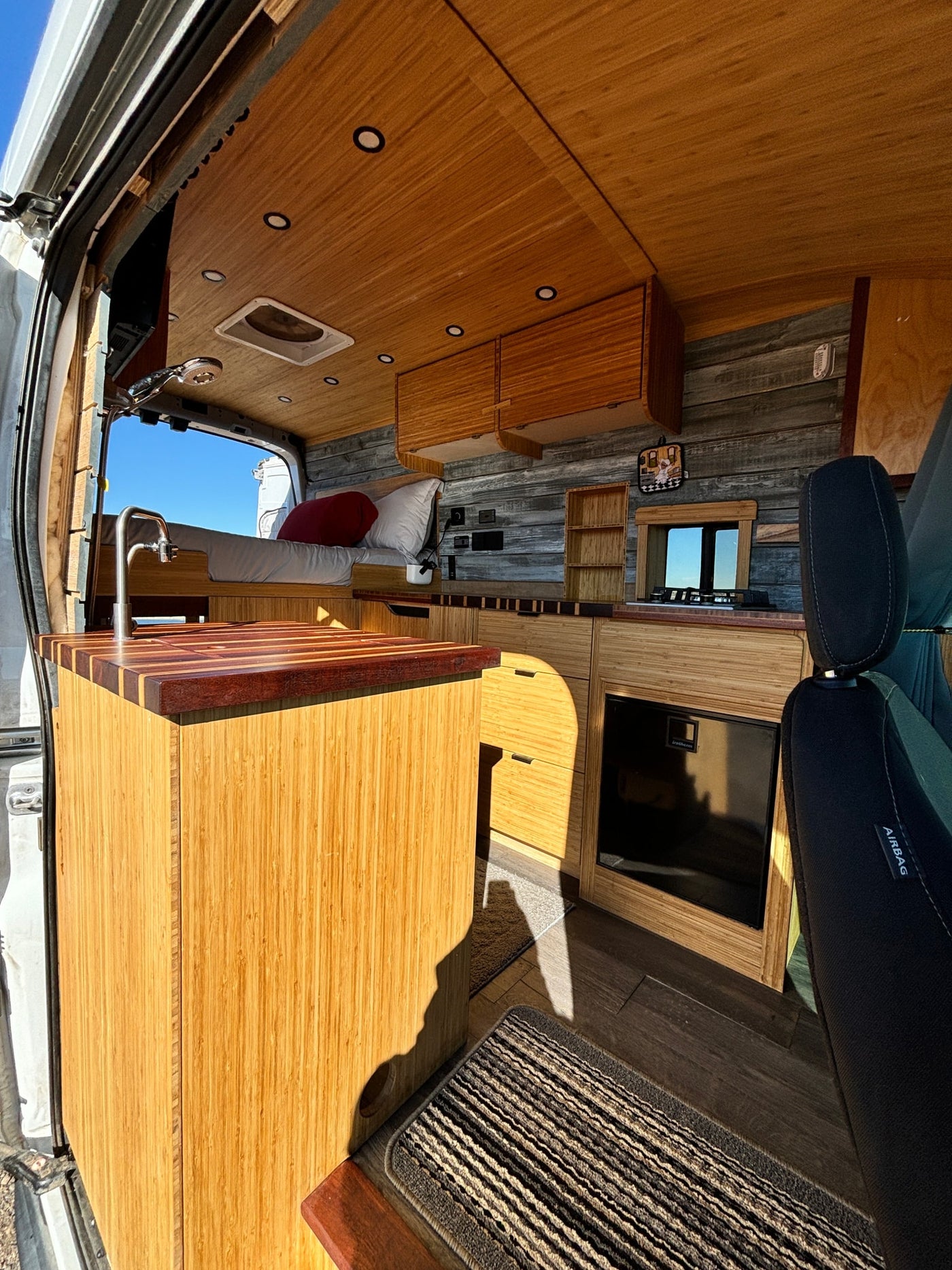 Step inside this custom bamboo RV rental, featuring a cozy bed, modern kitchen, and sleek wood interior for your next adventure. — photo 9