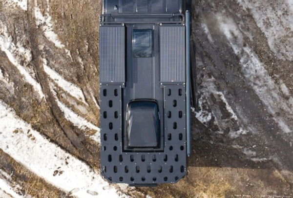 Overhead view of an RV rental: a dark grey overland vehicle with a large roof rack and storage panels on dirty snow.