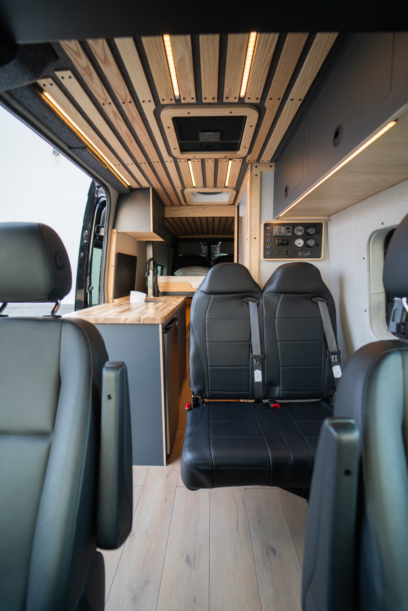 RV rental interior: A modern camper van with custom wood-slatted ceiling, LED lighting, sleek kitchen, and comfortable seating.