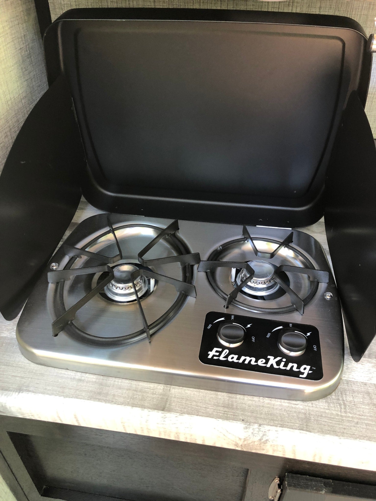 An RV rental features a compact FlameKing two-burner stove with a protective wind guard, ideal for camping.