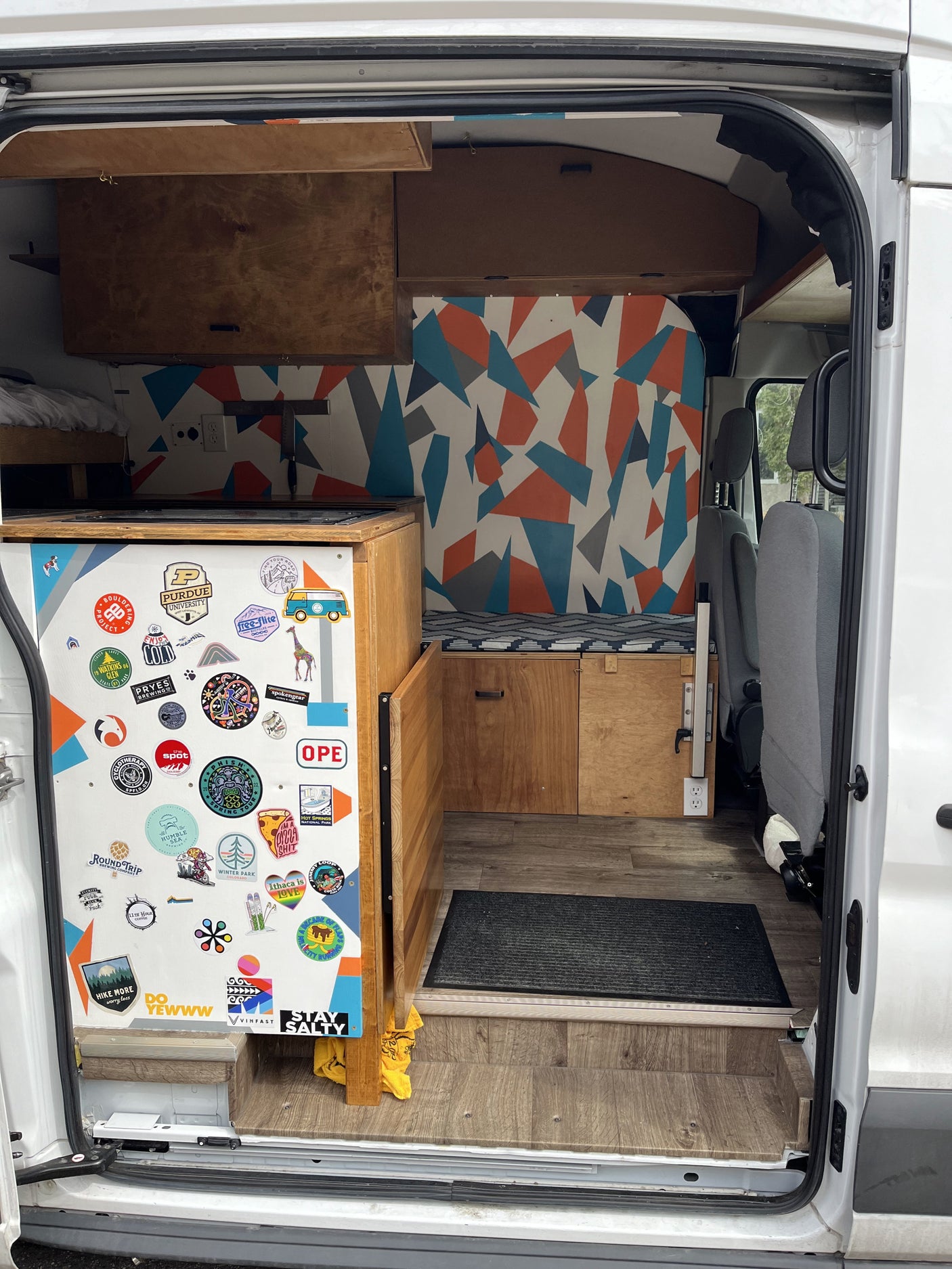 RV rental: Custom camper van interior with wood cabinetry, a colorful geometric wall, and a unique sticker collection.