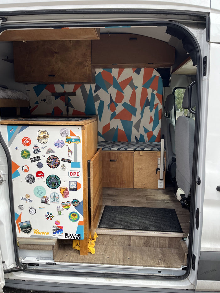 framed by bare trees on a paved lot.|RV rental: Custom camper van interior with wood cabinetry
