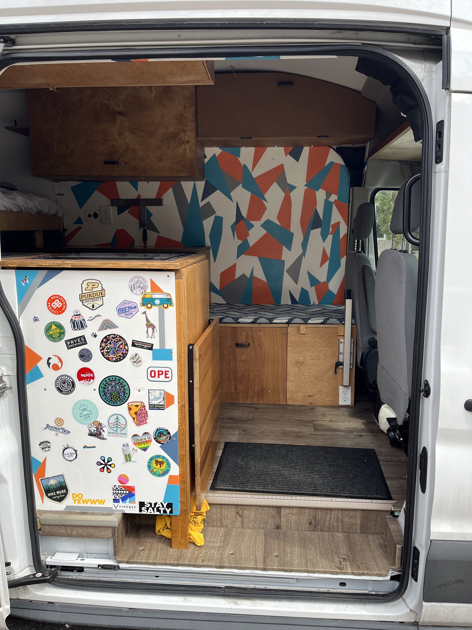 framed by bare trees on a paved lot.|RV rental: Custom camper van interior with wood cabinetry