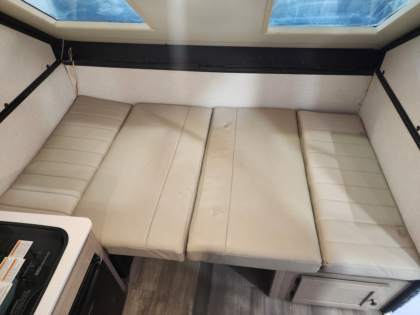 This RV rental interior features flexible light-colored cushions for seating/sleeping, a compact stove, and bright skylights. — photo 6