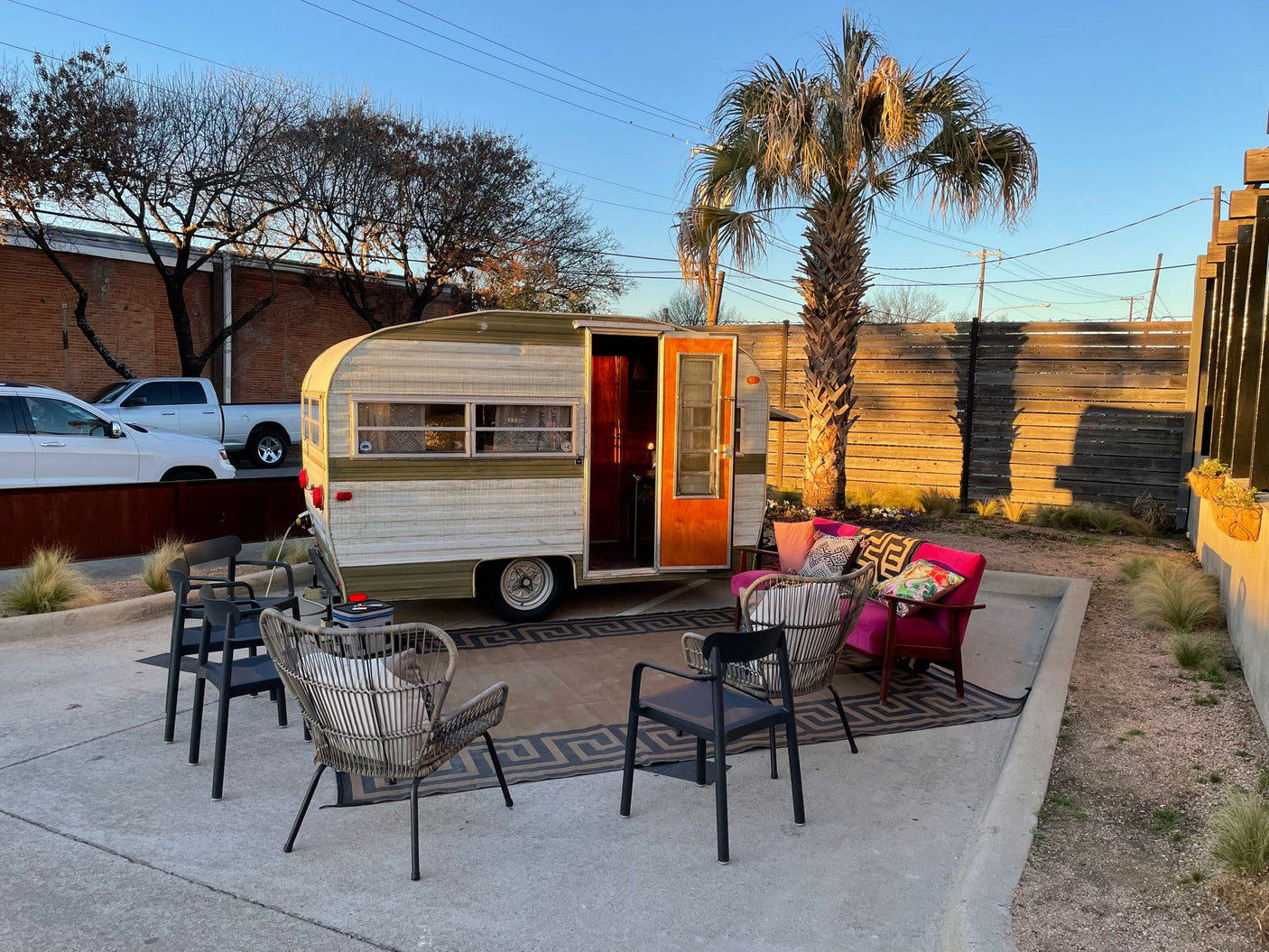 Experience a unique RV rental: a charming vintage camper with an inviting outdoor lounge area, rug, and a palm tree.