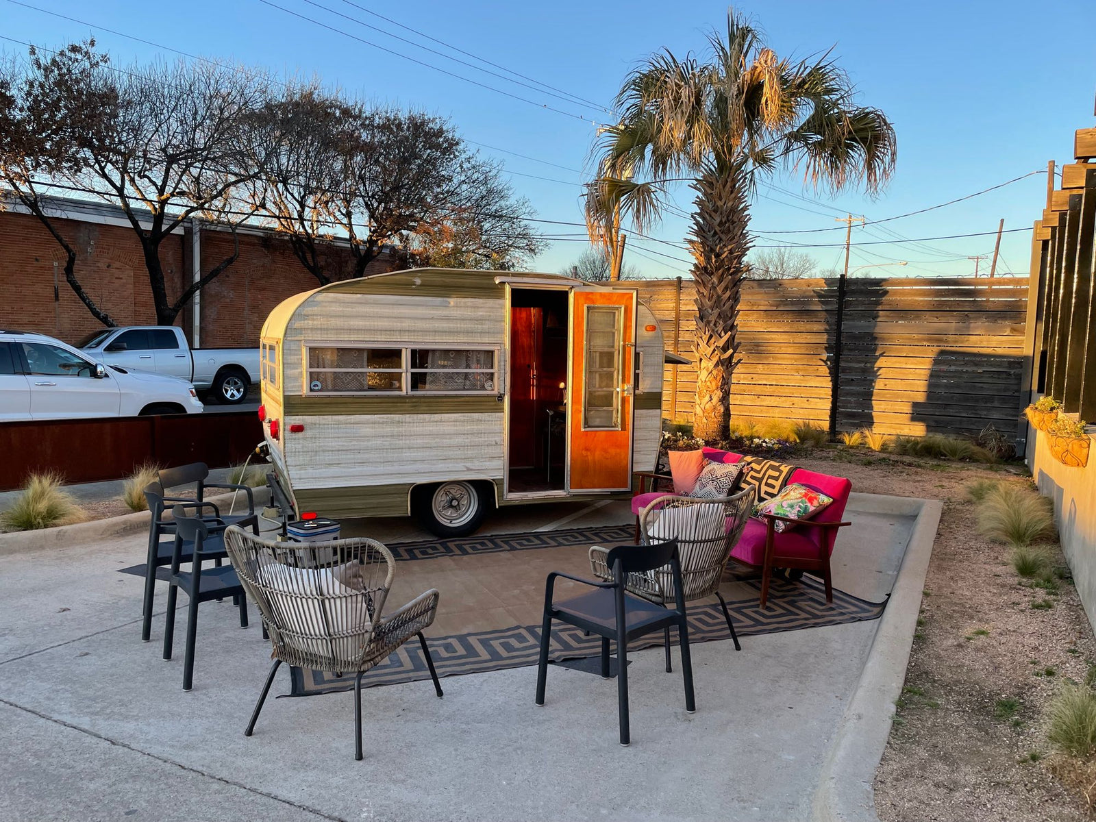 Experience a unique RV rental: a charming vintage camper with an inviting outdoor lounge area, rug, and a palm tree.